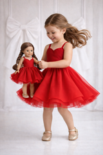 Young girl in a red dress holding a matching doll dress against a white background