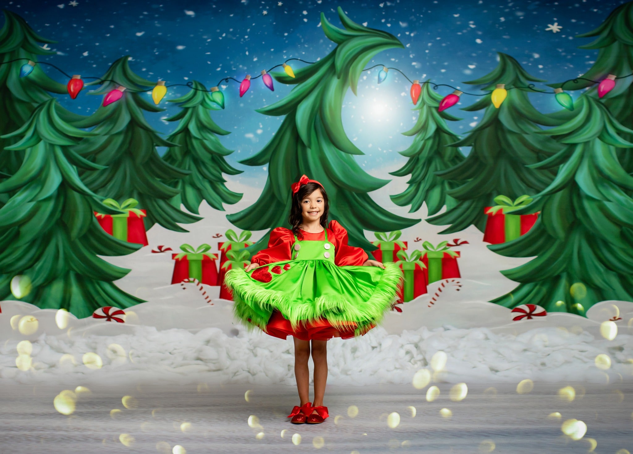 A little girl in a red and green dress with heart and candy designs holding hands with a boy in green suspenders and a matching bow tie.
