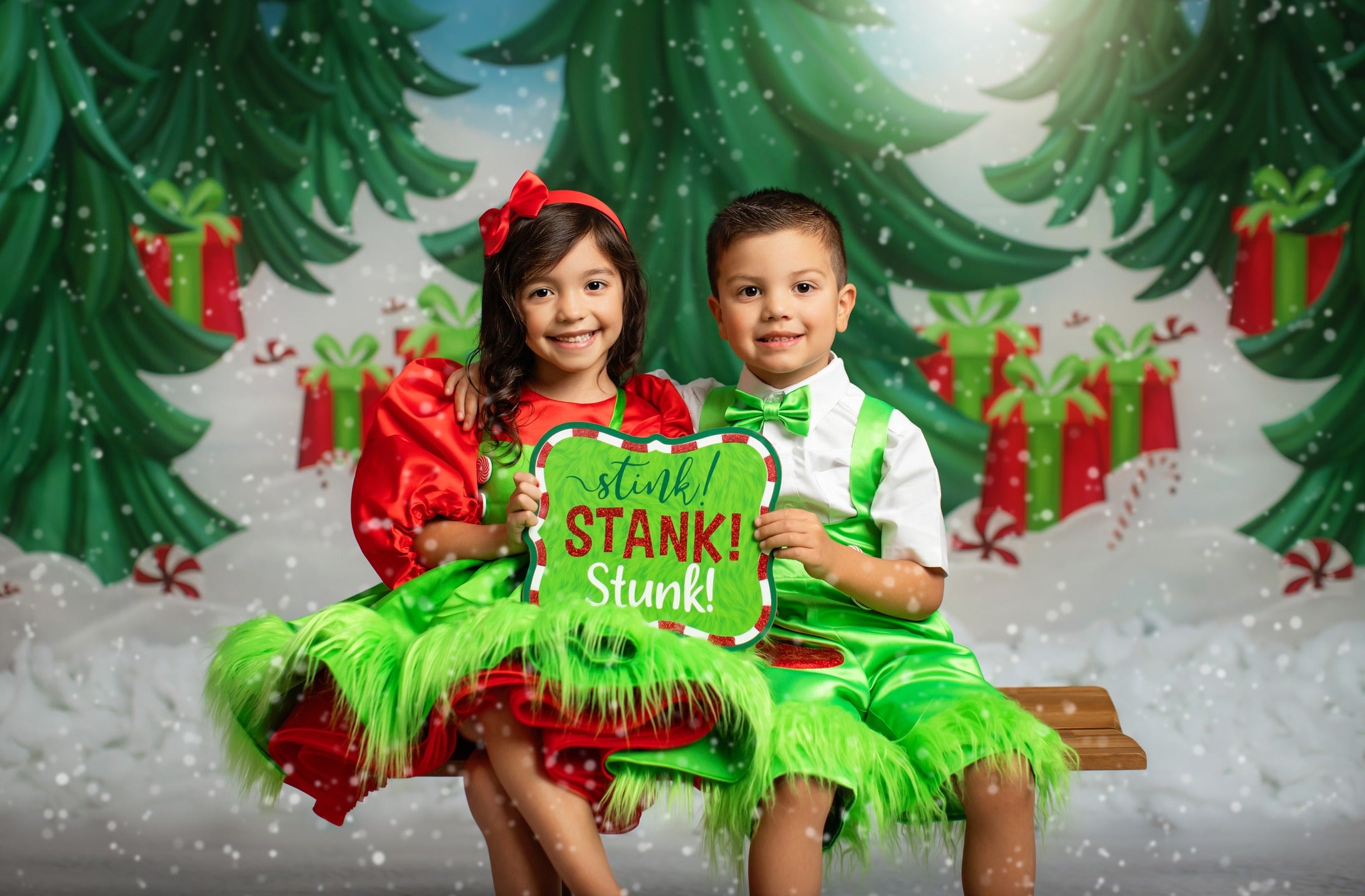 Siblings posing joyfully in coordinated holiday outfits, surrounded by a whimsical winter wonderland backdrop.
