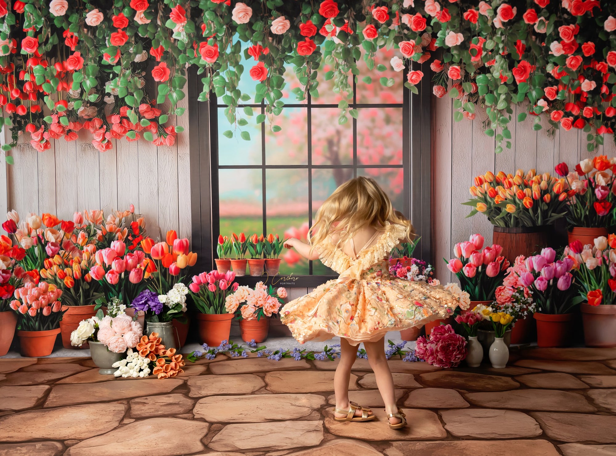 Child in a floral dress standing in front of a wall decorated with flowers and plants.