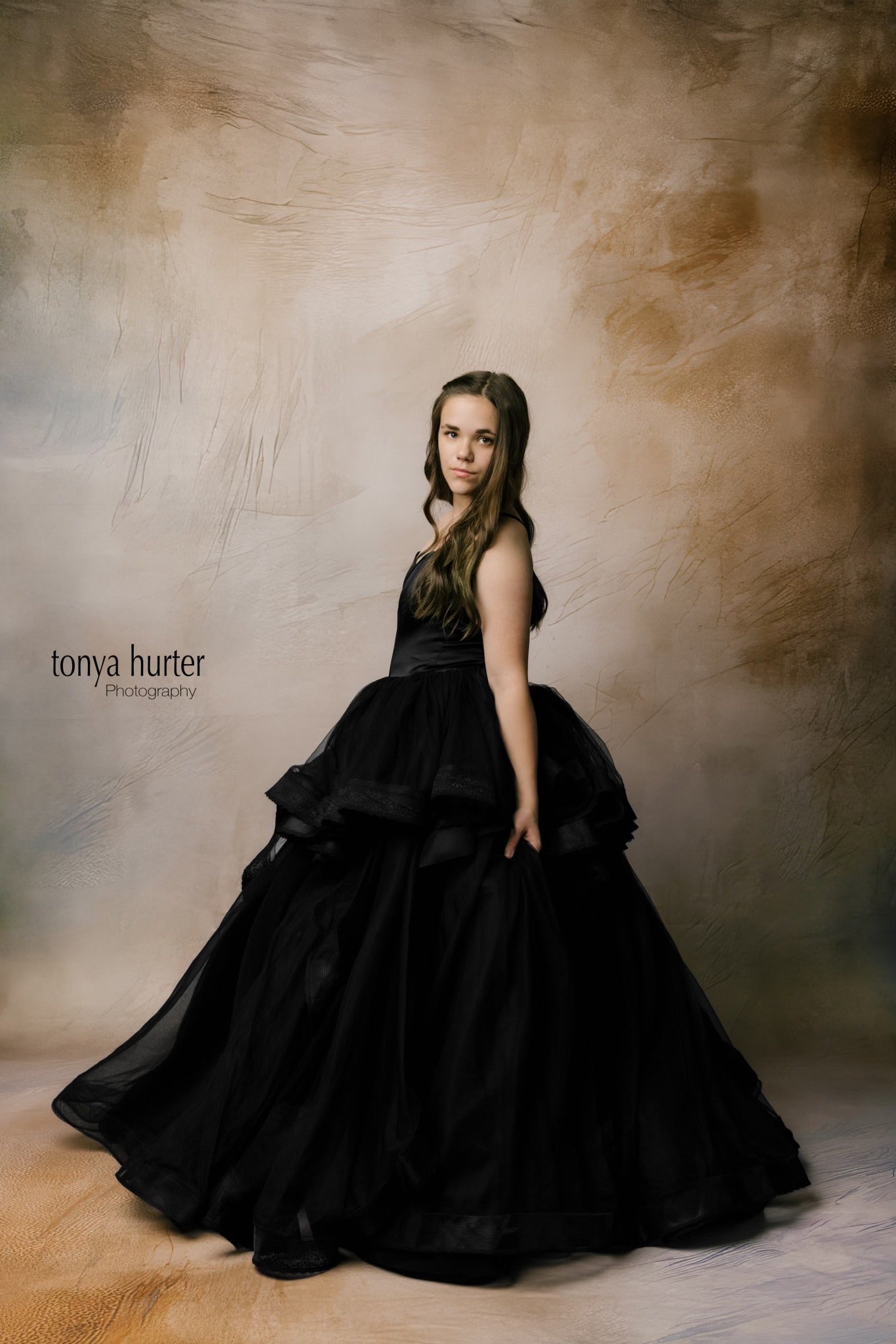 "Side view of a girl in a timeless black gown, showcasing a floor-length skirt and a detailed lace back."
