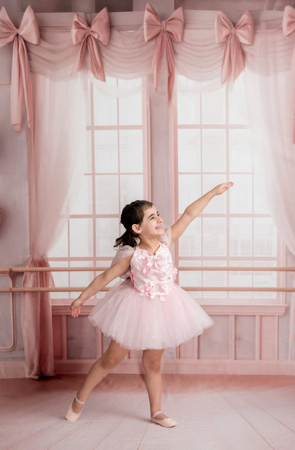 Young girl in a ballet outfit dancing in a pink ballet studio with decorative bows on the windows.