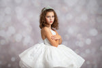 Young girl in a white dress with a tiara against a blurred light background