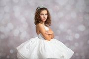 Young girl in a white dress with a tiara against a blurred light background