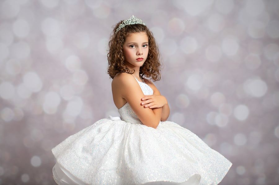 Young girl in a white dress with a tiara against a blurred light background