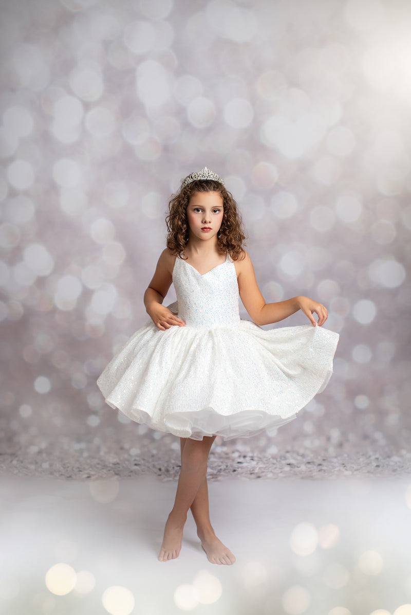 Young girl in a white dress with a tiara against a blurred light background