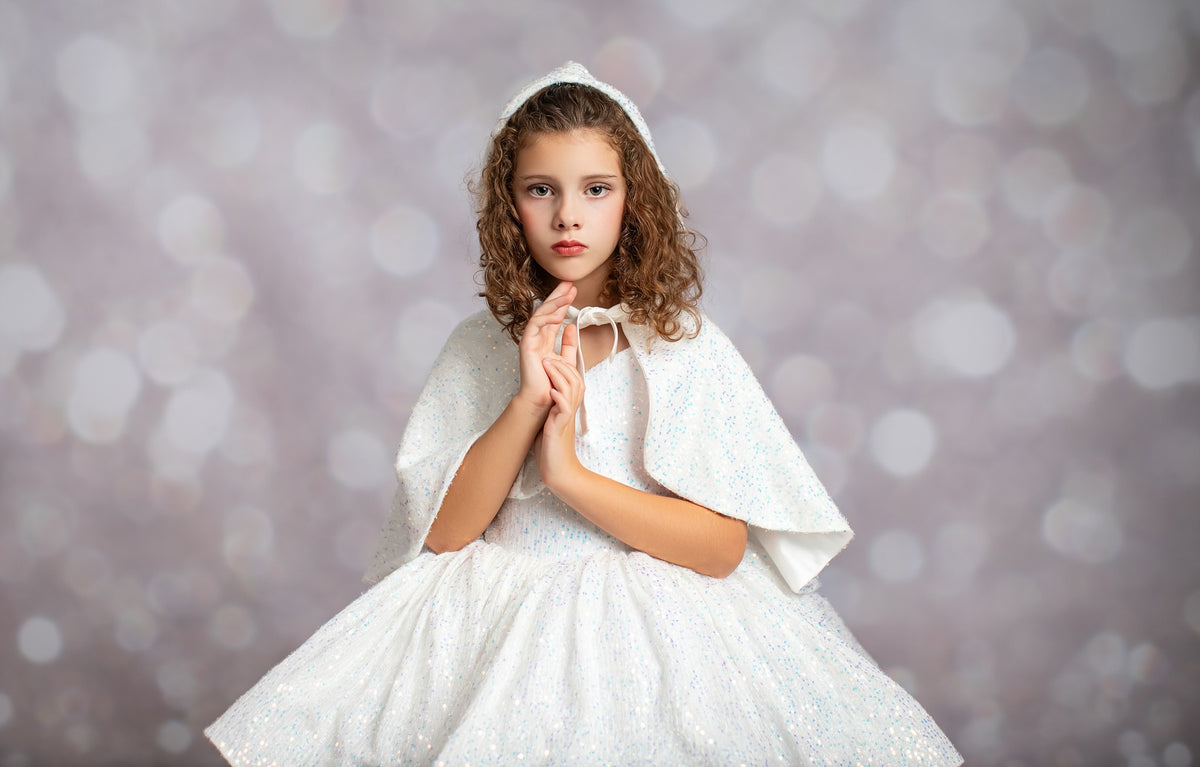 Young girl in a white dress with a hood against a blurred background