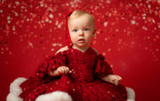 Baby in a red sequin dress sitting on a red background with snowflake patterns