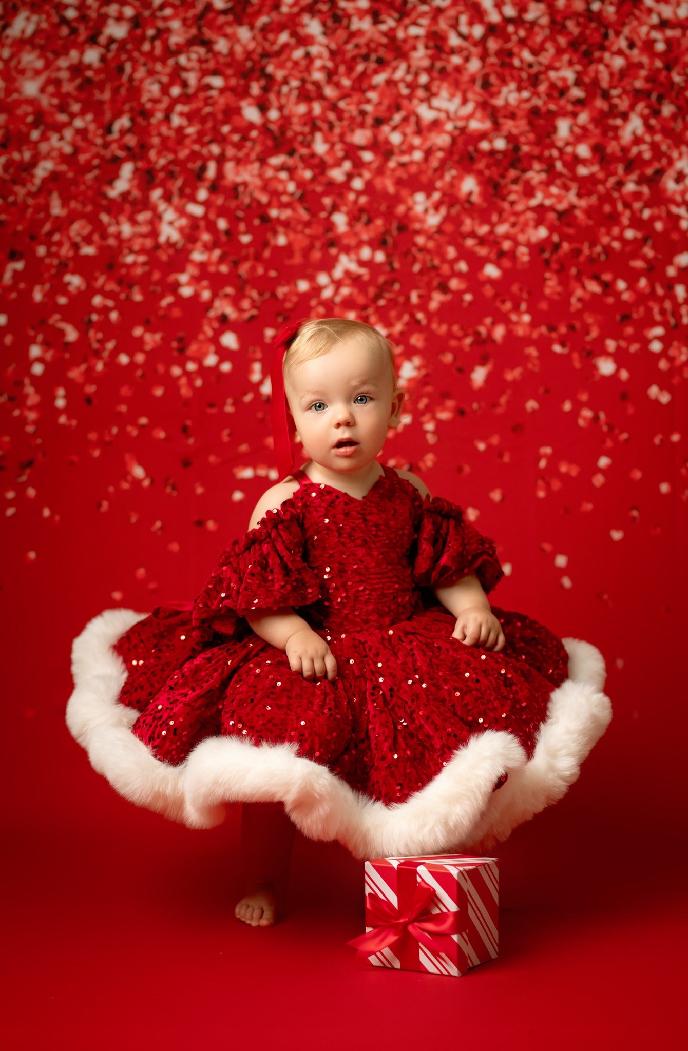 Baby in a red dress sitting on a white cushion with a red background