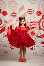 Young girl in a red dress holding a gift box against a candy-themed backdrop