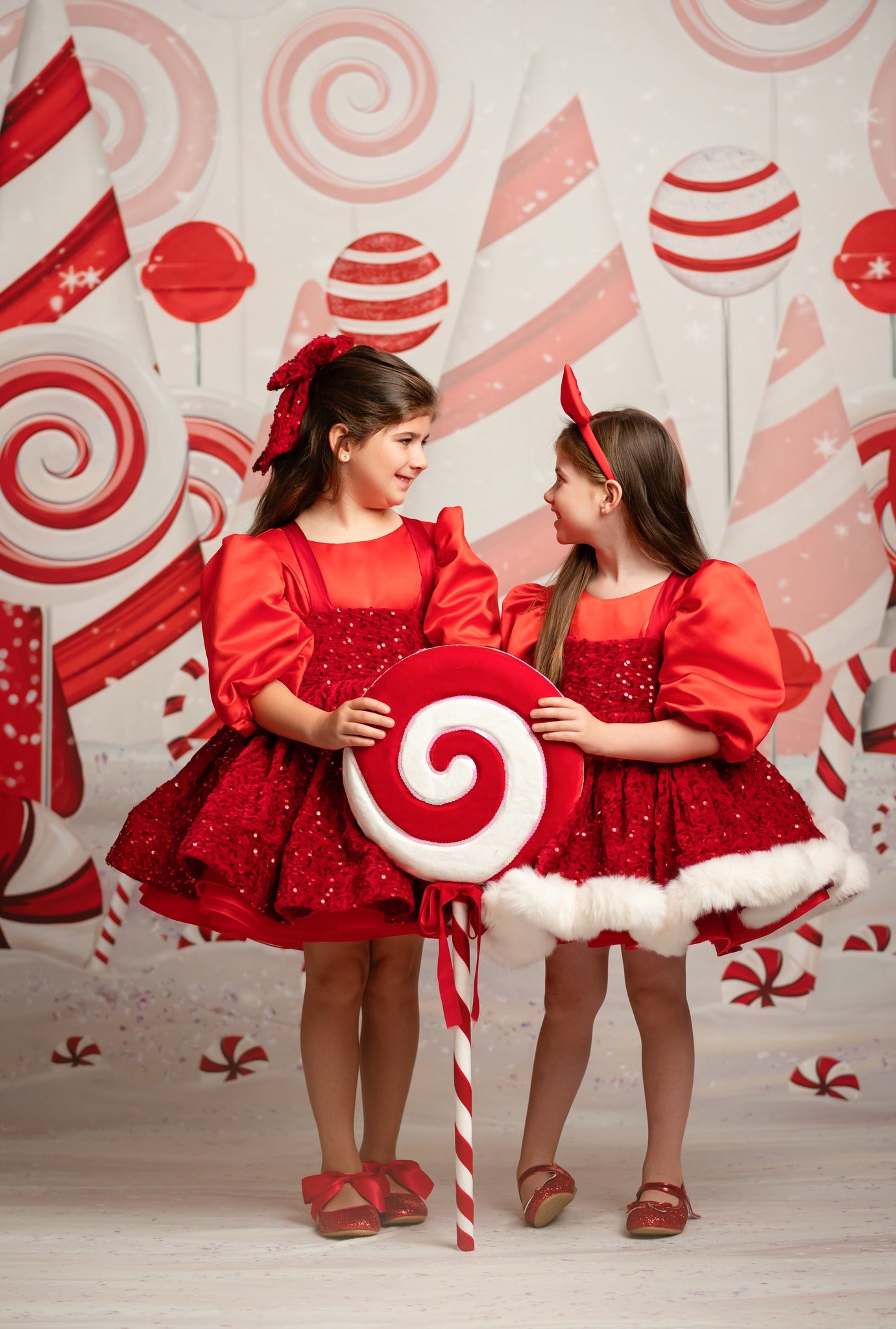 Two children in red outfits with candy cane props against a candy-themed backdrop