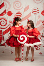 Two children in red outfits with candy cane props against a candy-themed backdrop