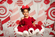 Child in a red dress with a large bow sitting in front of a candy-themed background