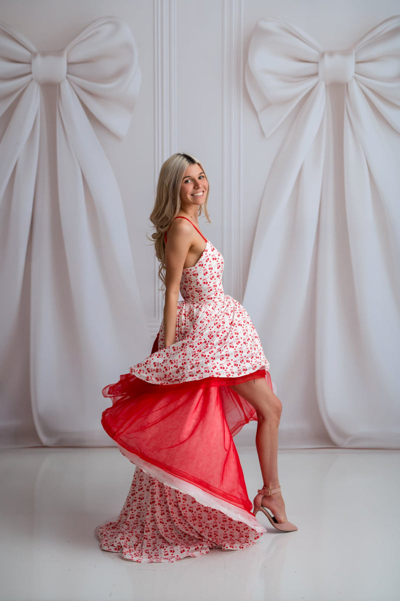 Woman in a red and white floral dress standing against a white wall with large decorative bows.