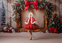 Girl standing outdoors in the red velvet holiday gown and cape, framed by winter trees and golden hour light.

