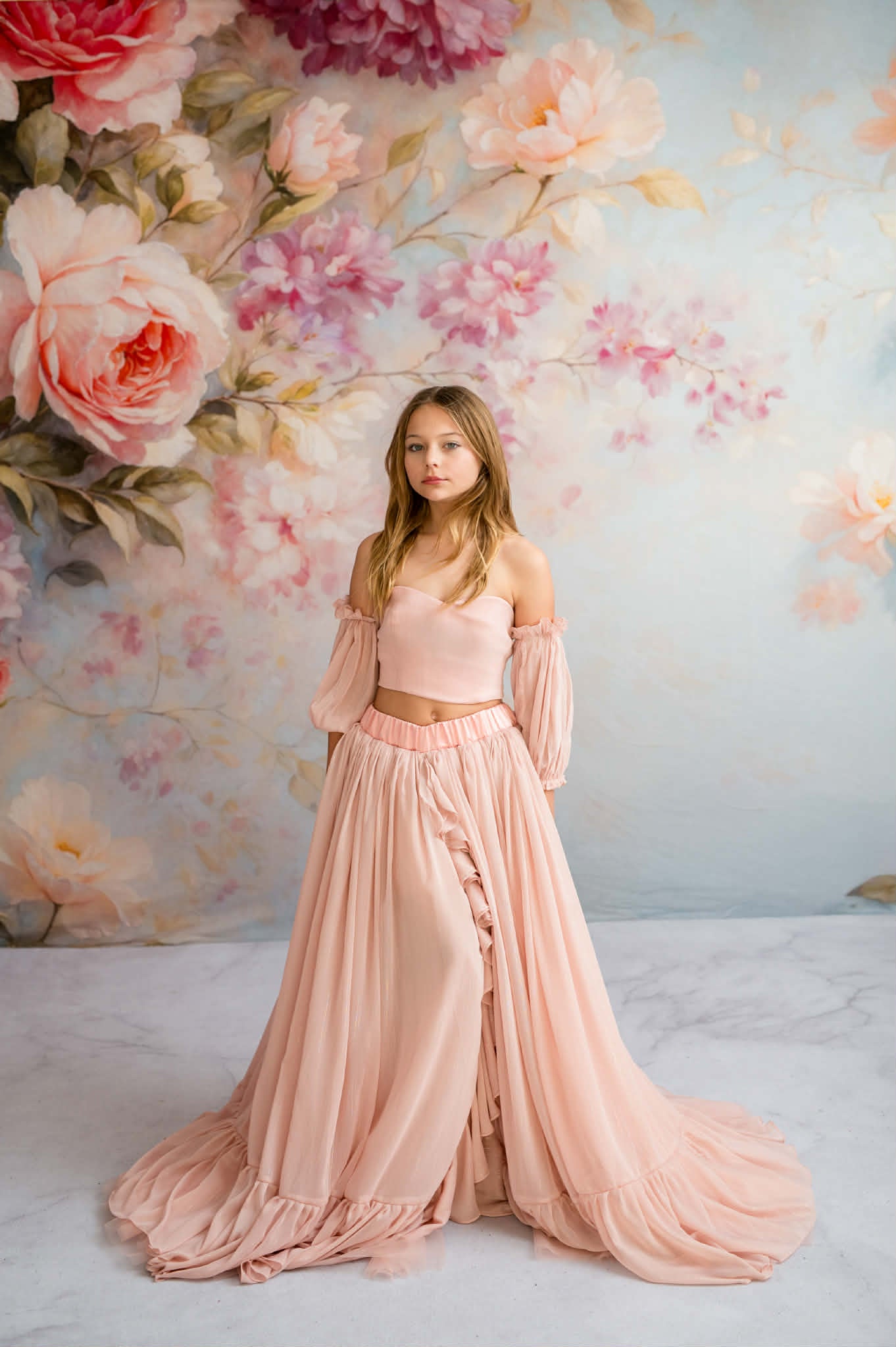 Woman in a pink dress standing against a floral wall.