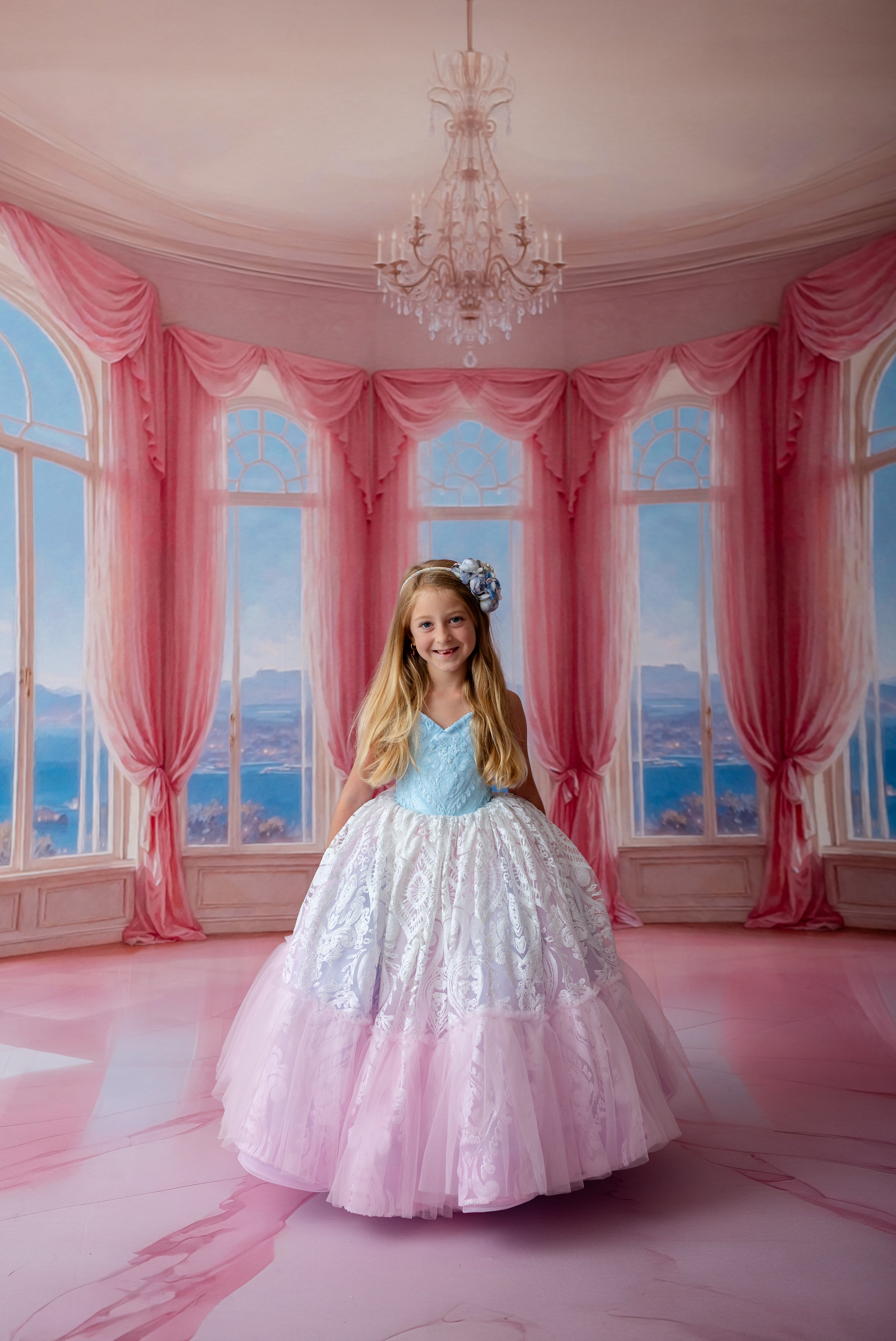 Young girl in a white and pink dress standing in a room with pink curtains and a chandelier.