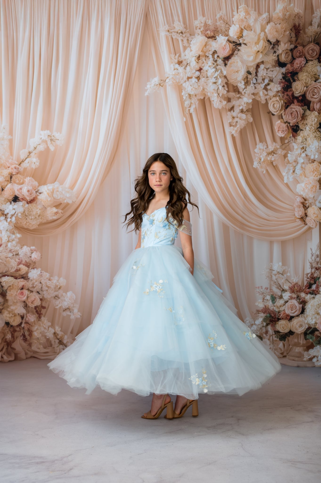 Young girl in a light blue dress standing in front of floral decorations