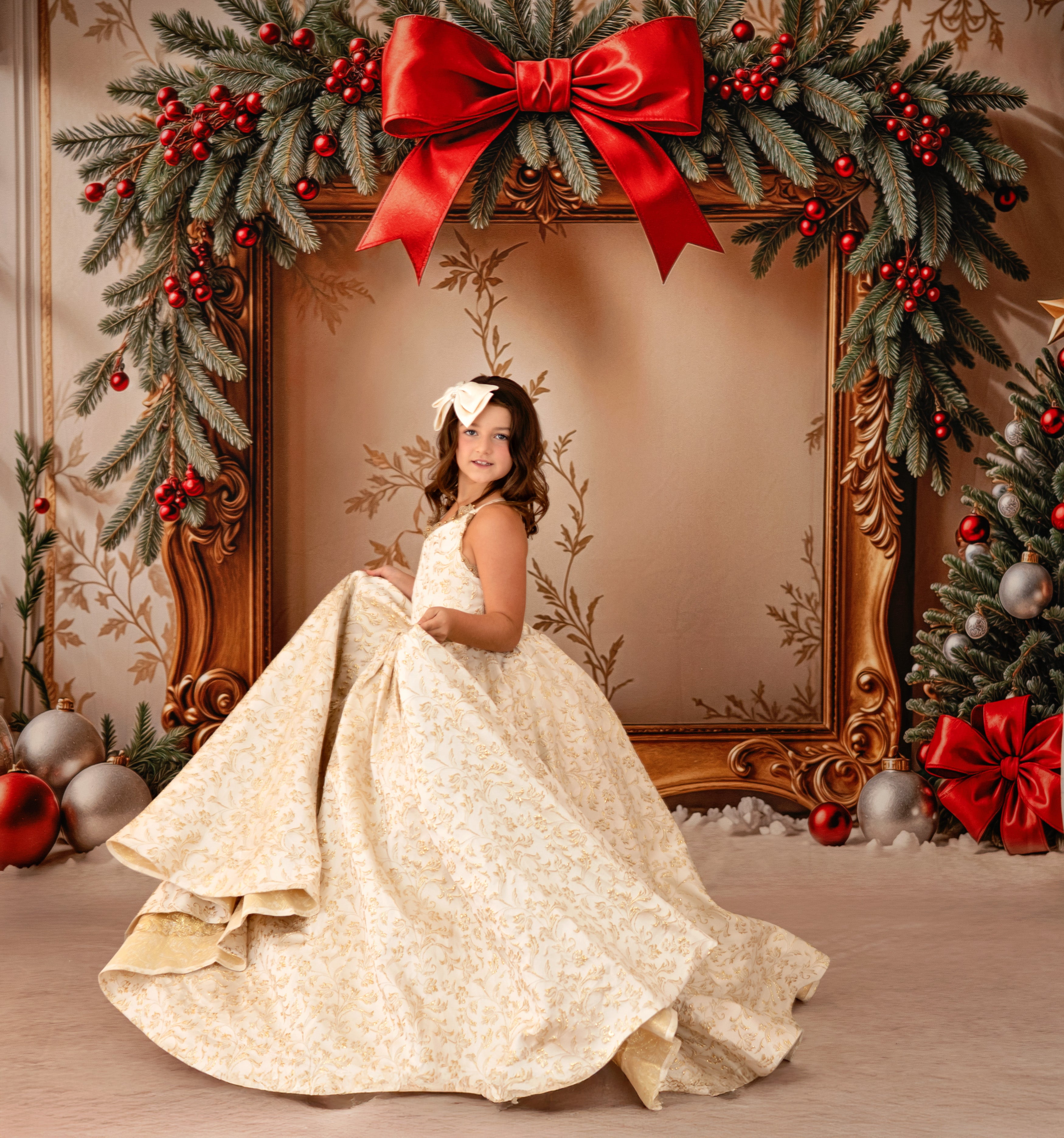 Young girl in a white dress standing in front of a decorated Christmas frame with red bows and greenery.