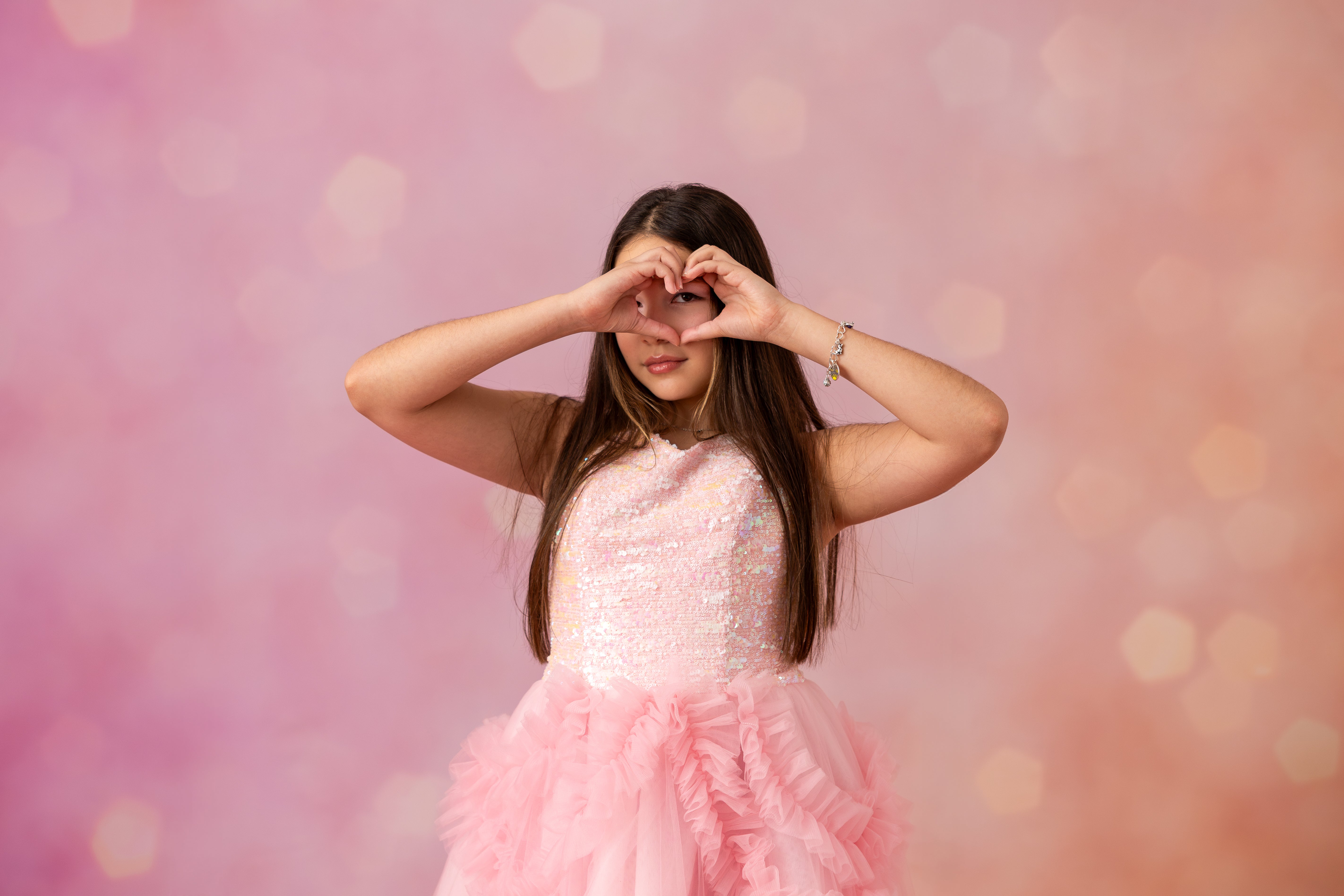 Woman in a pink dress making a heart shape with her hands against a pink background