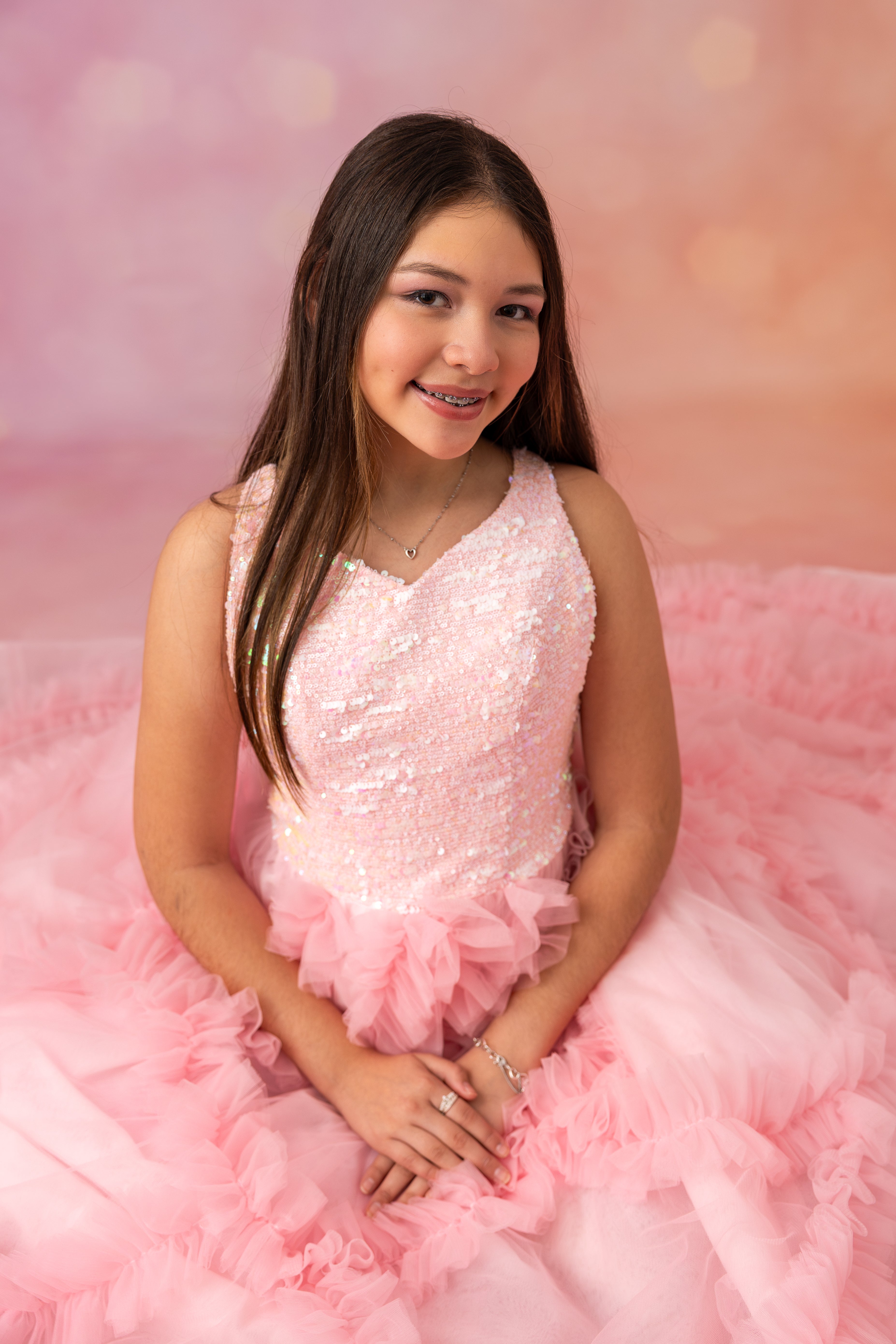 Young woman in a pink dress sitting on a pink fluffy surface with a soft pink background