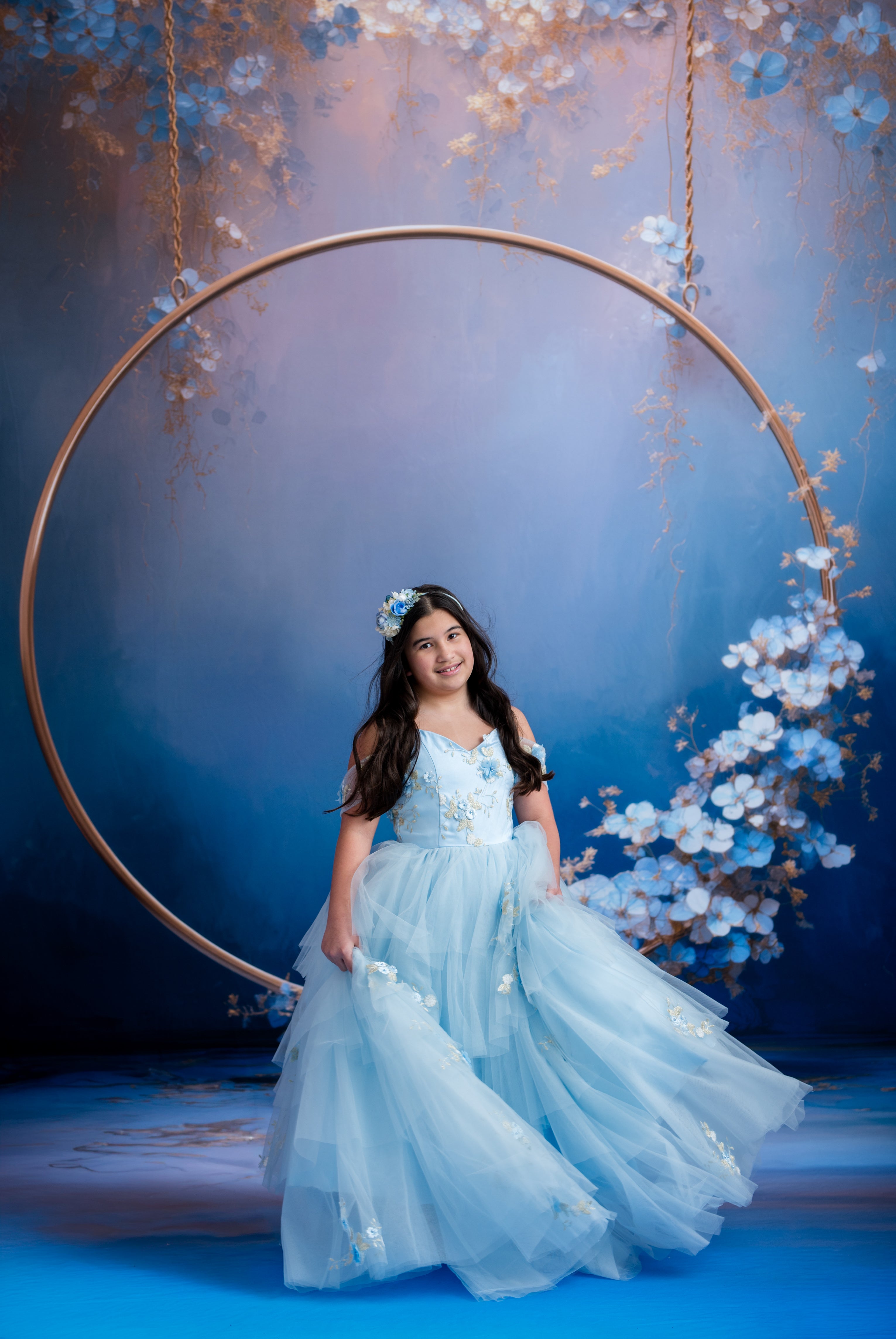 Young girl in a light blue dress standing in front of a floral arch with a dark blue background