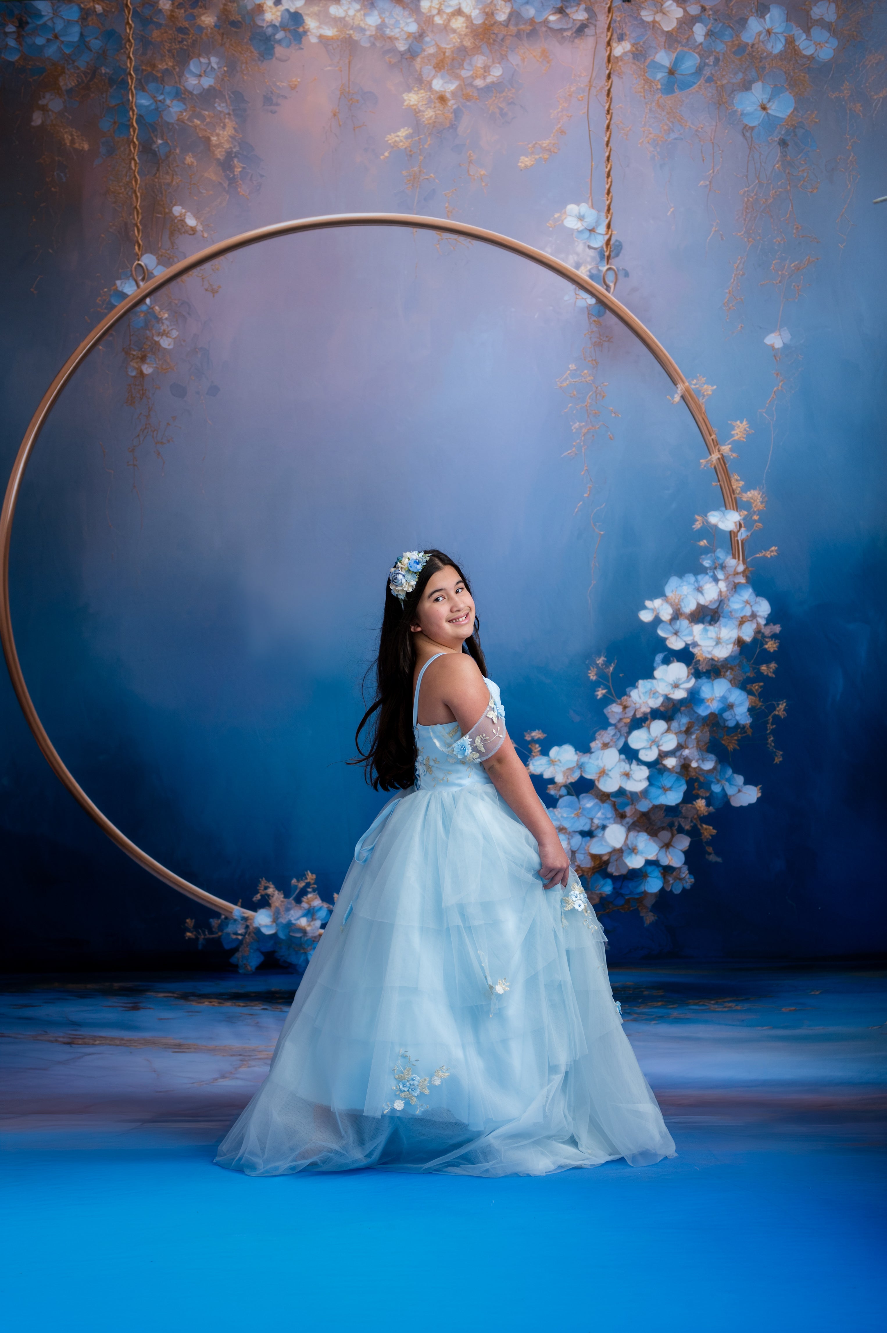 Woman in a light blue dress sitting on a floral swing against a dark blue background