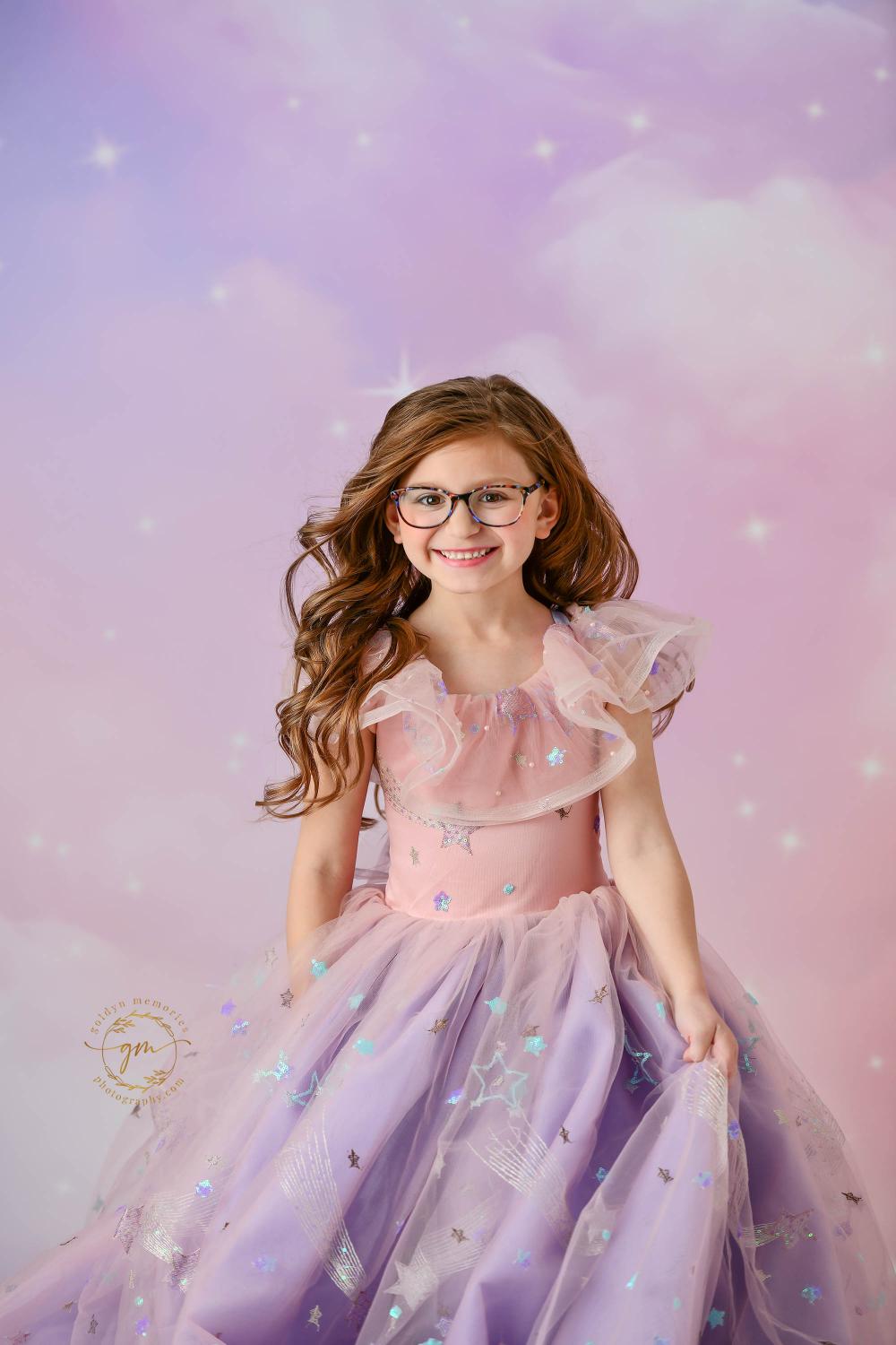 "A fairytale-inspired photo of a girl in a ruffled pastel dress adorned with shimmering stars, standing against a soft, cloudy background."

