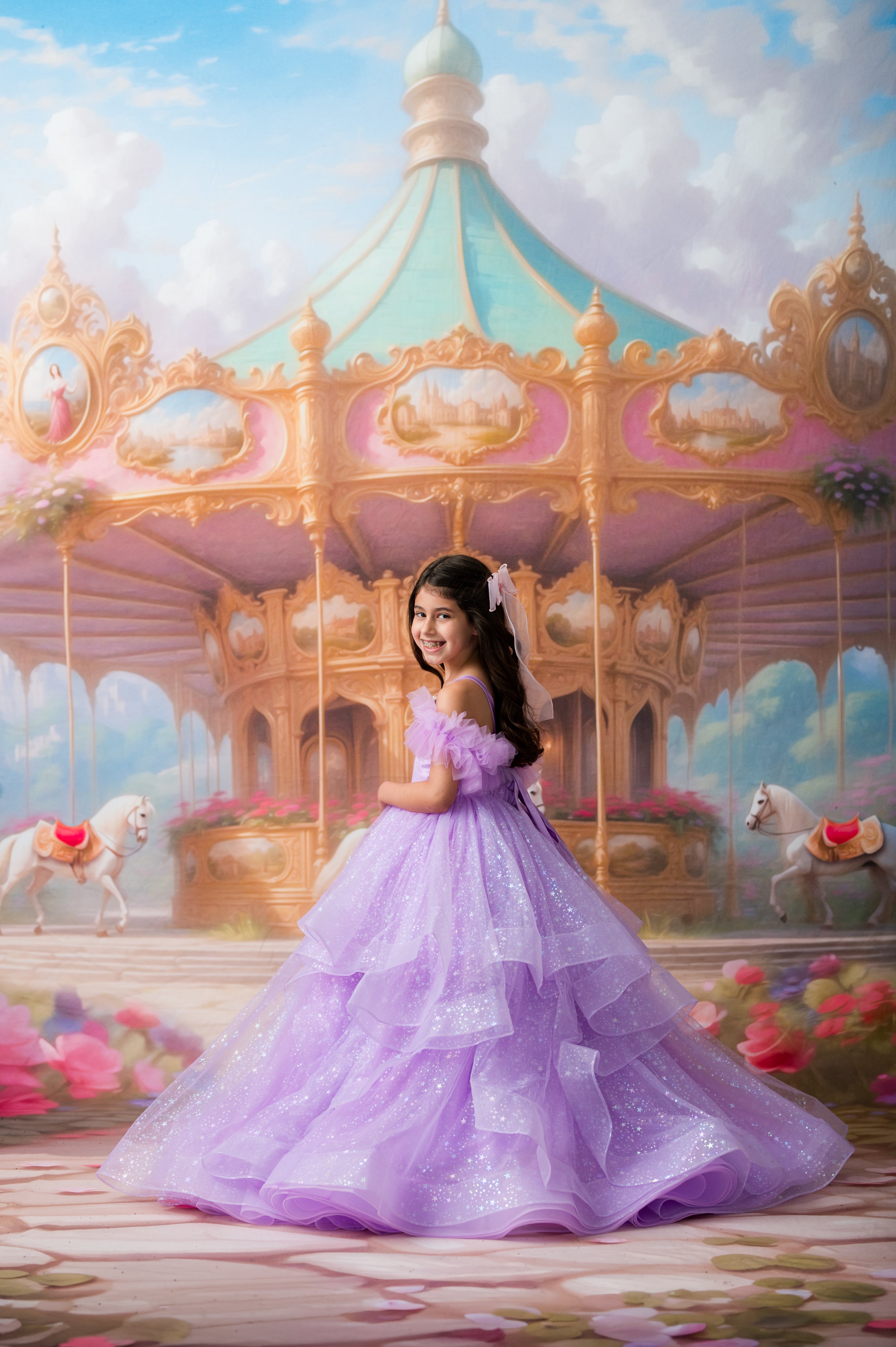 A young girl in a sparkling lavender ball gown stands in front of an ornate pastel carousel under a soft blue sky with clouds.