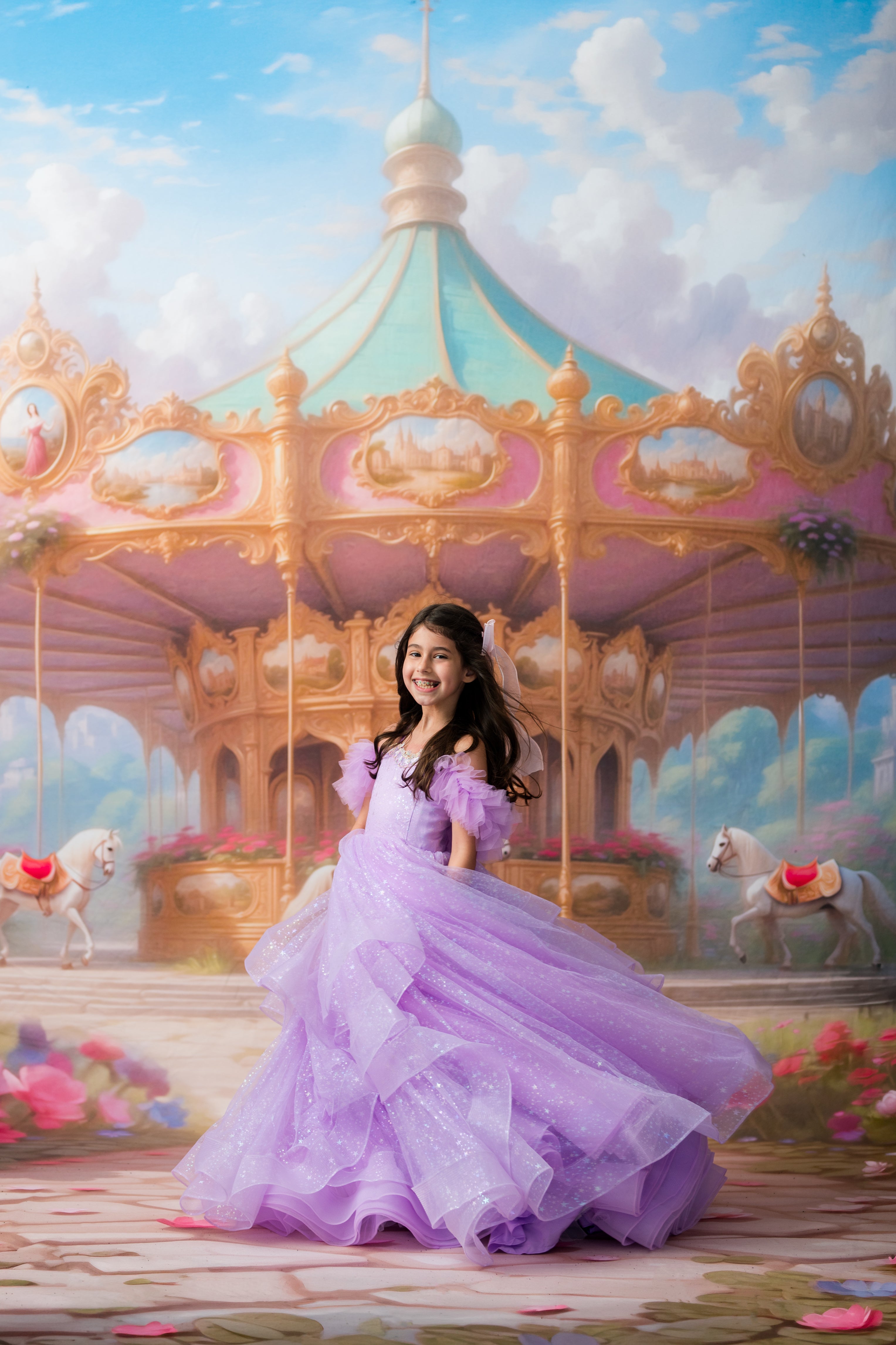 A young girl in a voluminous lavender tulle ball gown stands in front of a pastel carousel under a blue sky with clouds.
