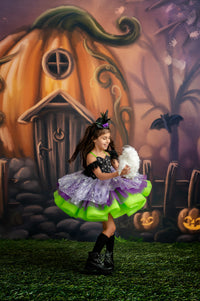 Child in a Halloween costume standing in front of a pumpkin house with pumpkins and ghosts in the background.