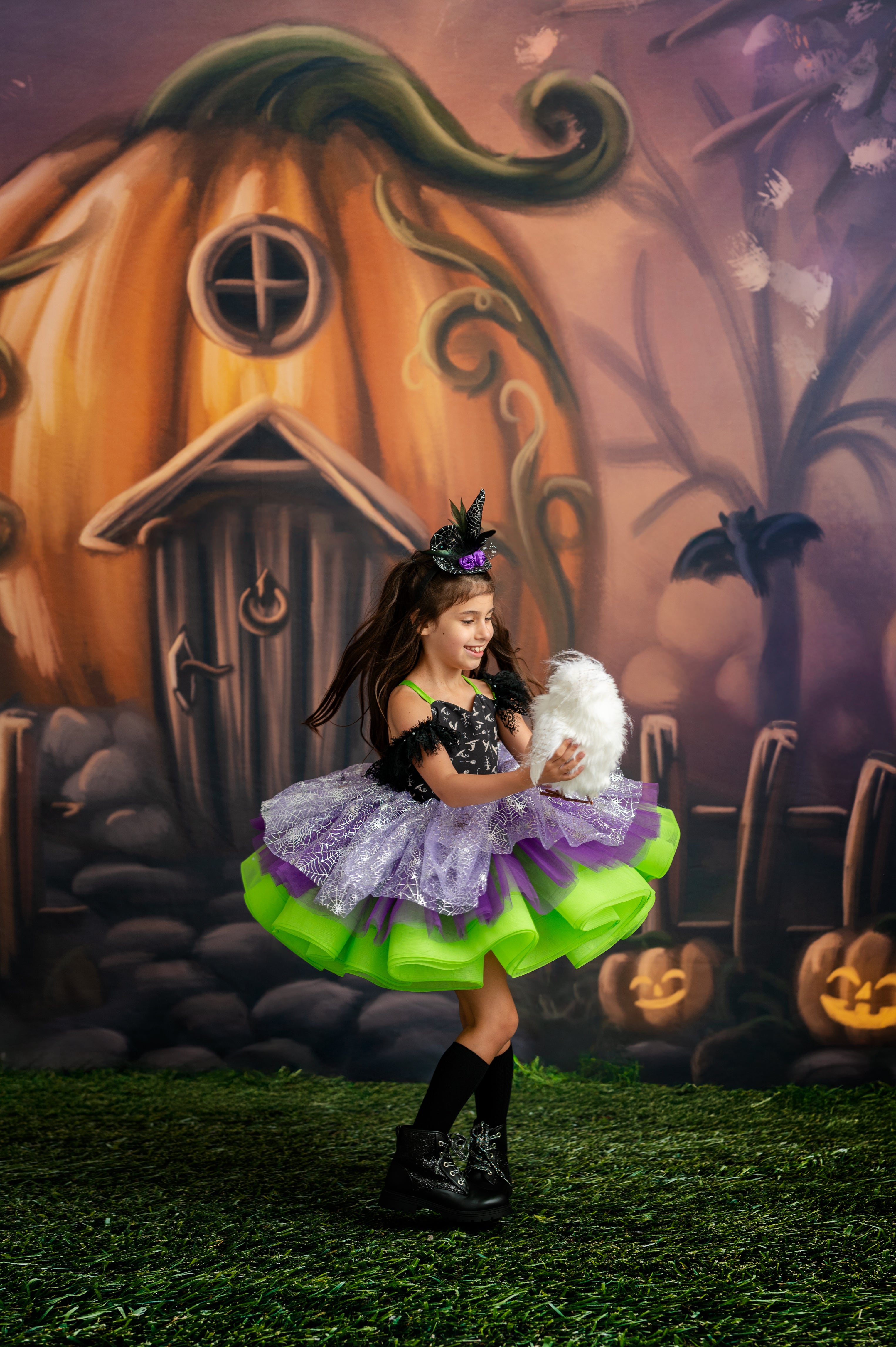 Child in a Halloween costume standing in front of a pumpkin house with pumpkins and ghosts in the background.