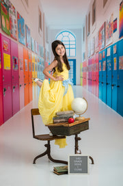 Young girl in a yellow dress standing in a colorful school hallway with lockers.