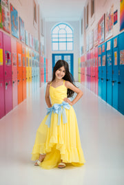 Young girl in a yellow dress with a blue bow standing in a colorful hallway.