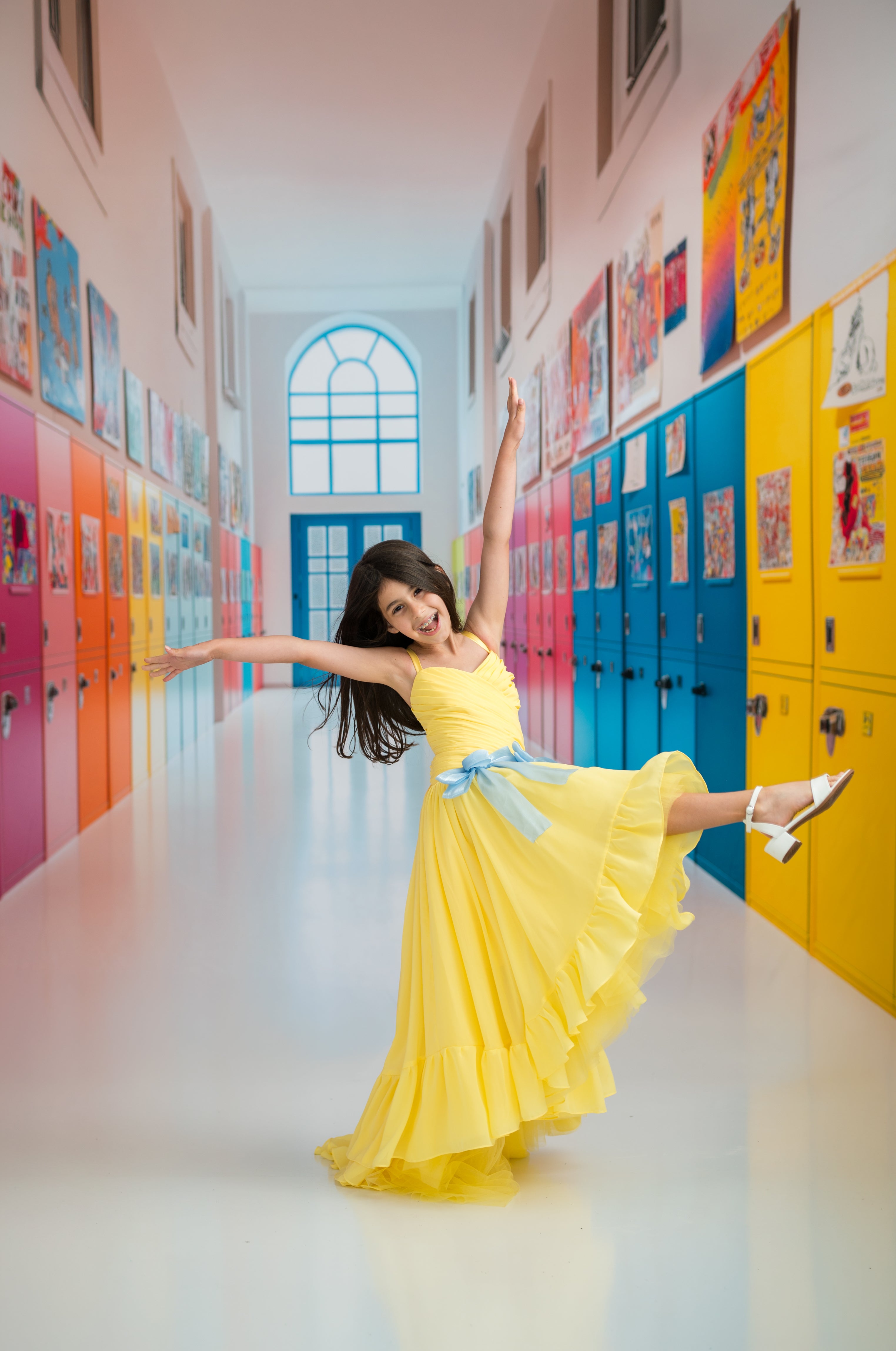 Young girl in a yellow dress posing in a colorful school hallway.