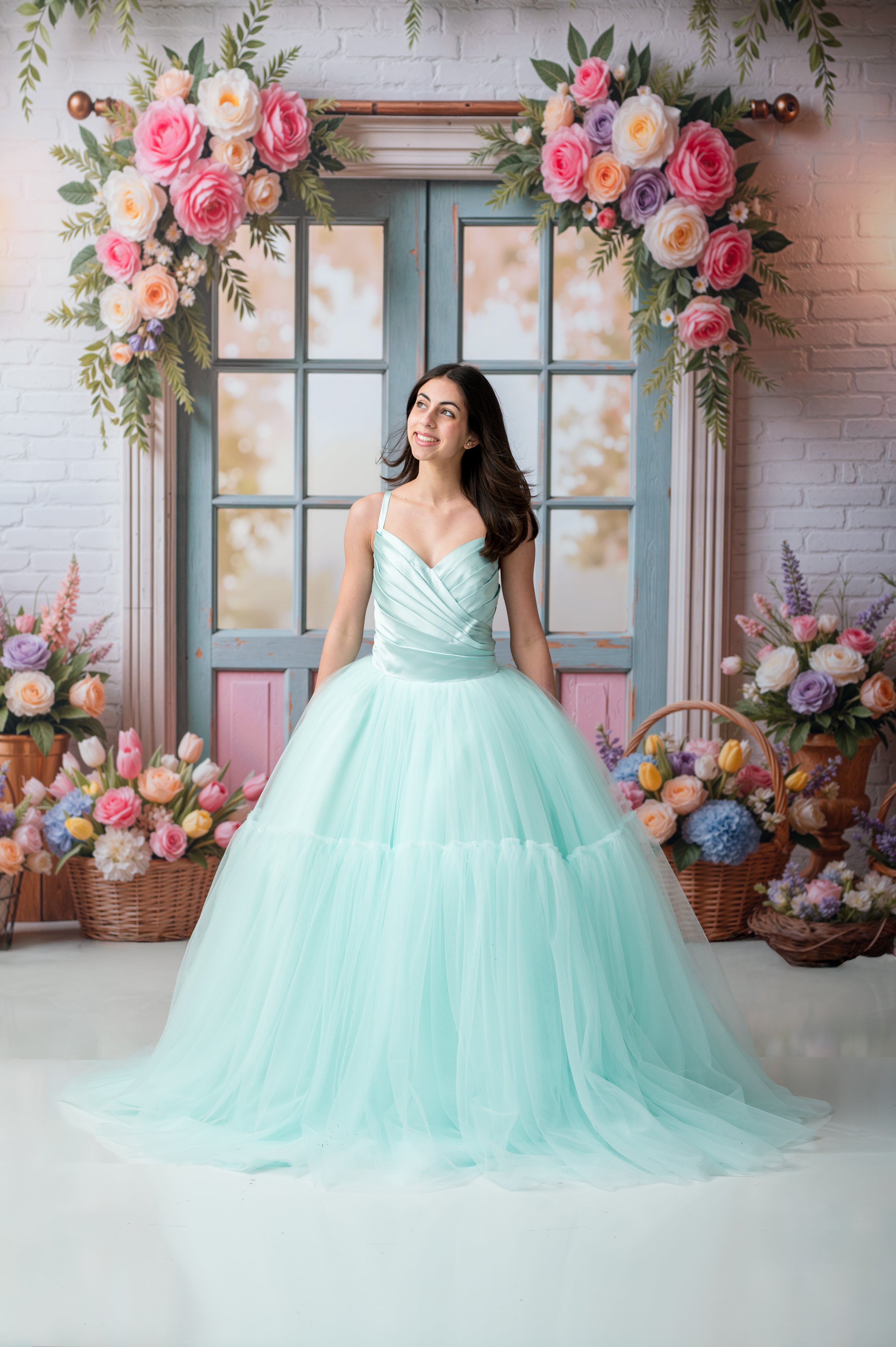 Woman in a light blue dress standing in front of a decorated wall with flowers and a door.