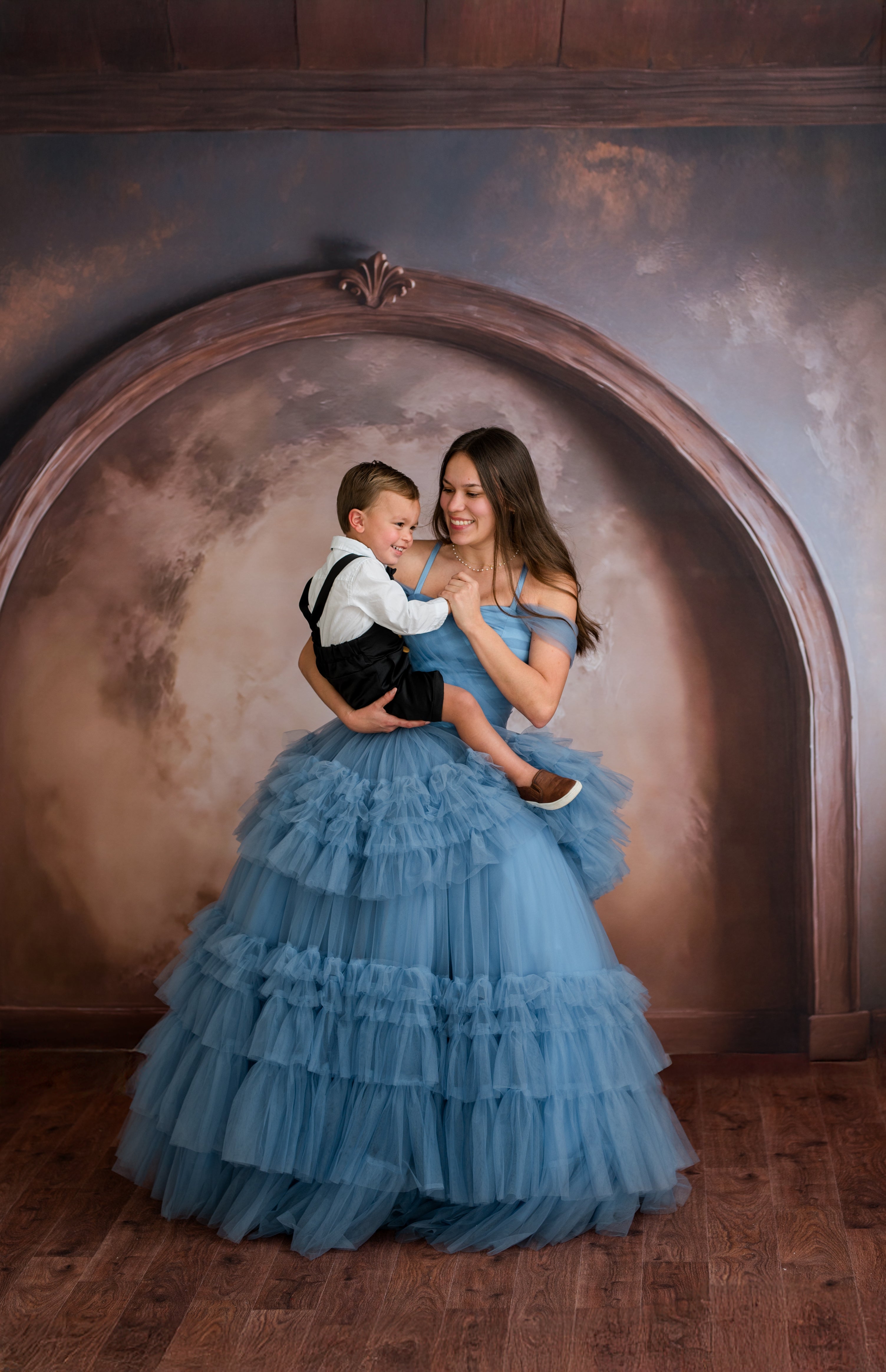 Woman in a blue dress holding a child against a decorative wall.