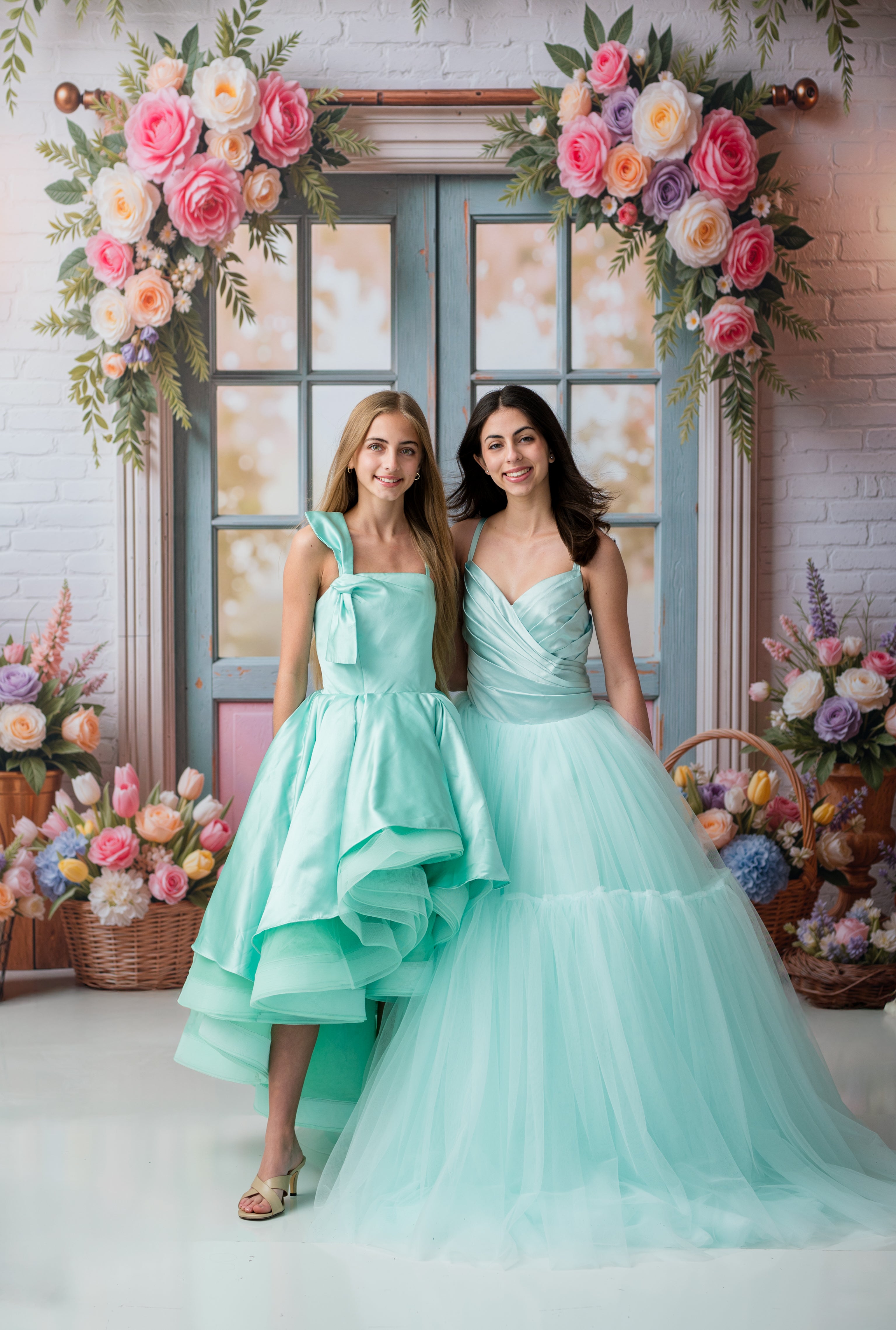 Two women in mint green dresses standing in front of a floral arch.