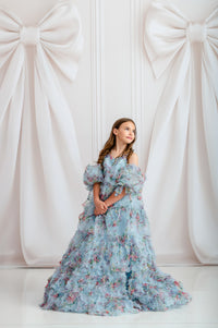 Girl wearing Fancy Mae floral blue chiffon gown with puff sleeves and bows

