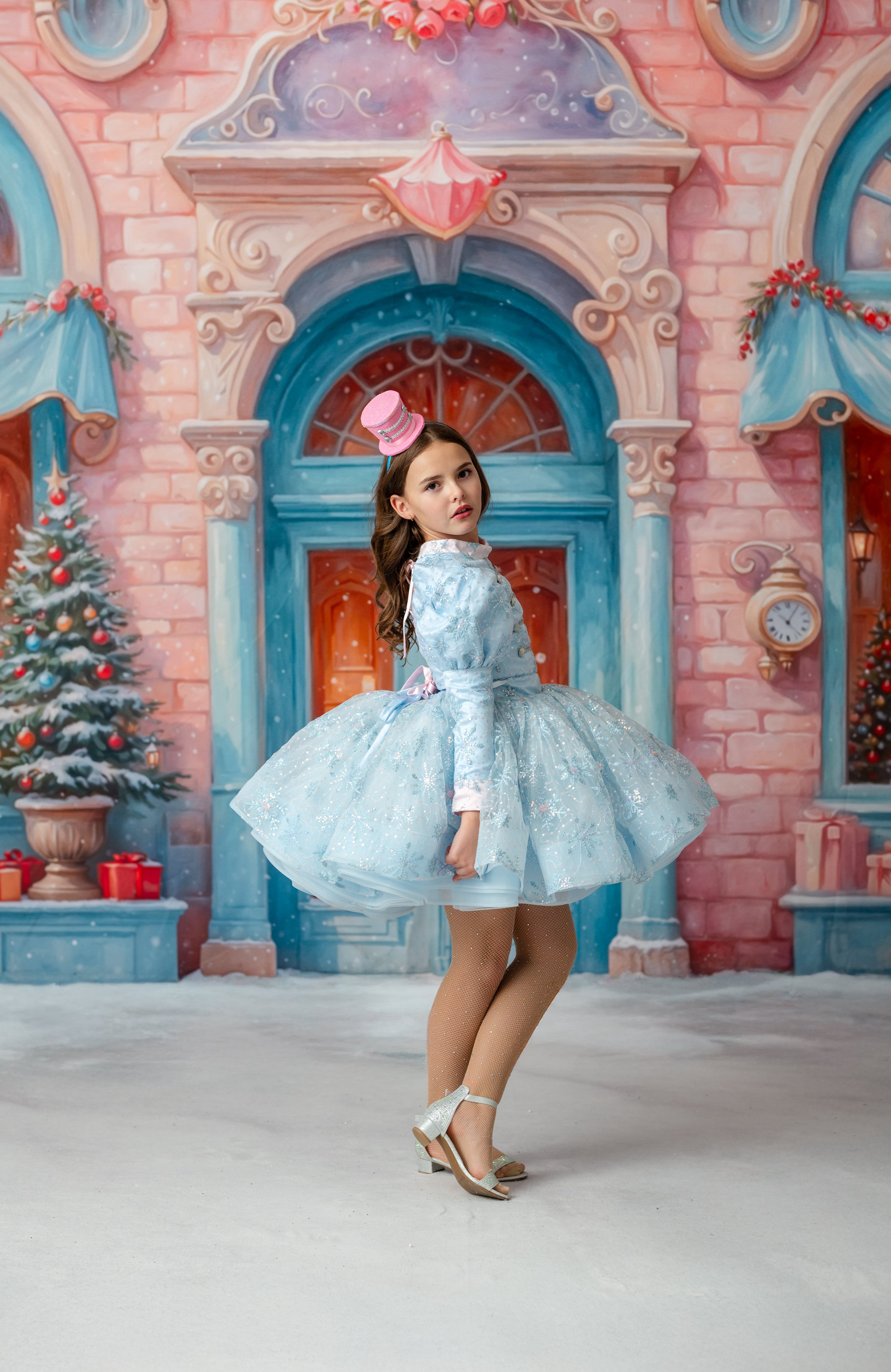 Young girl in a blue dress standing in front of a fairy-tale castle with Christmas decorations.