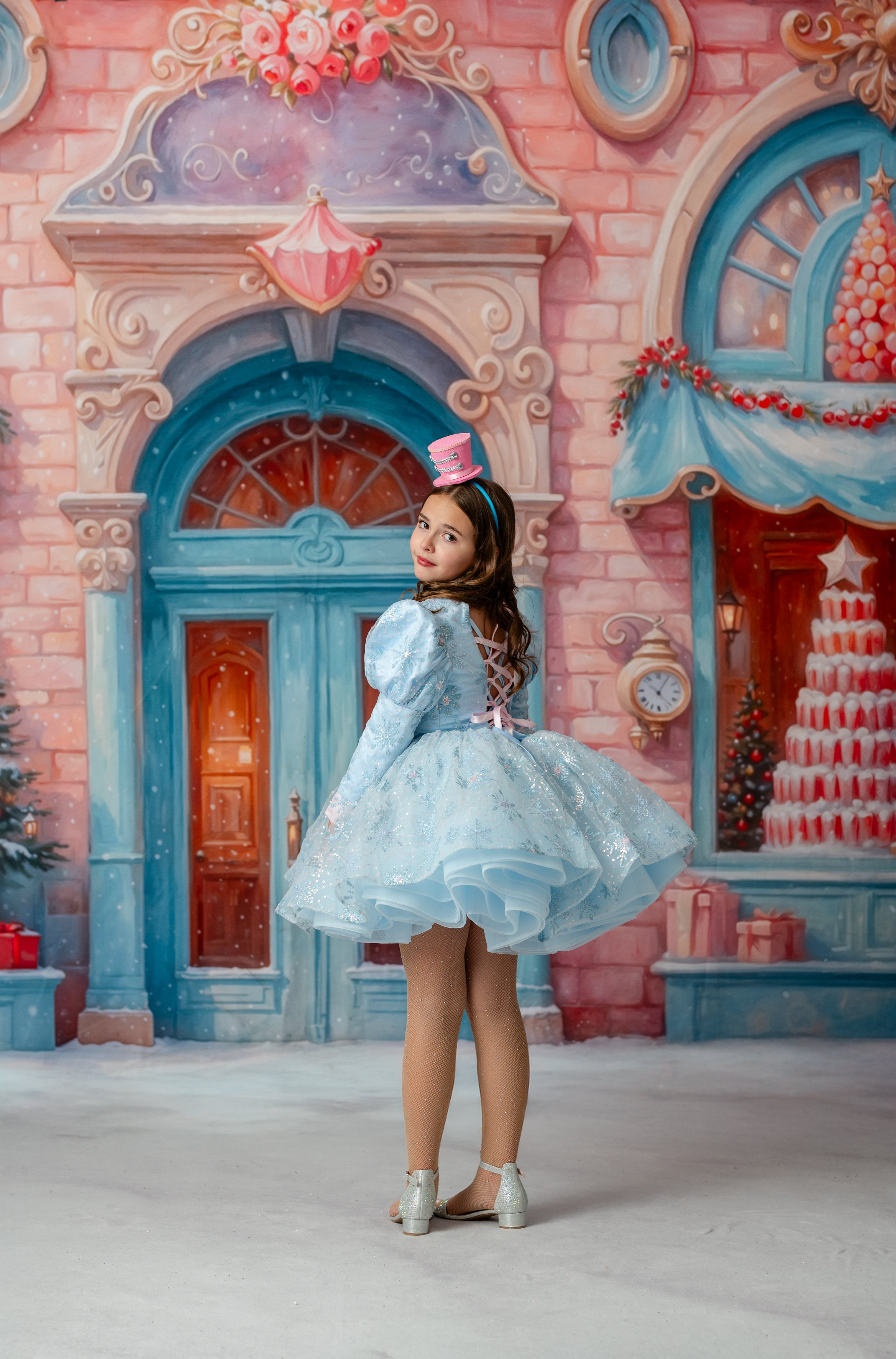 Young girl in a blue dress standing in front of a colorful, fantasy-style building.