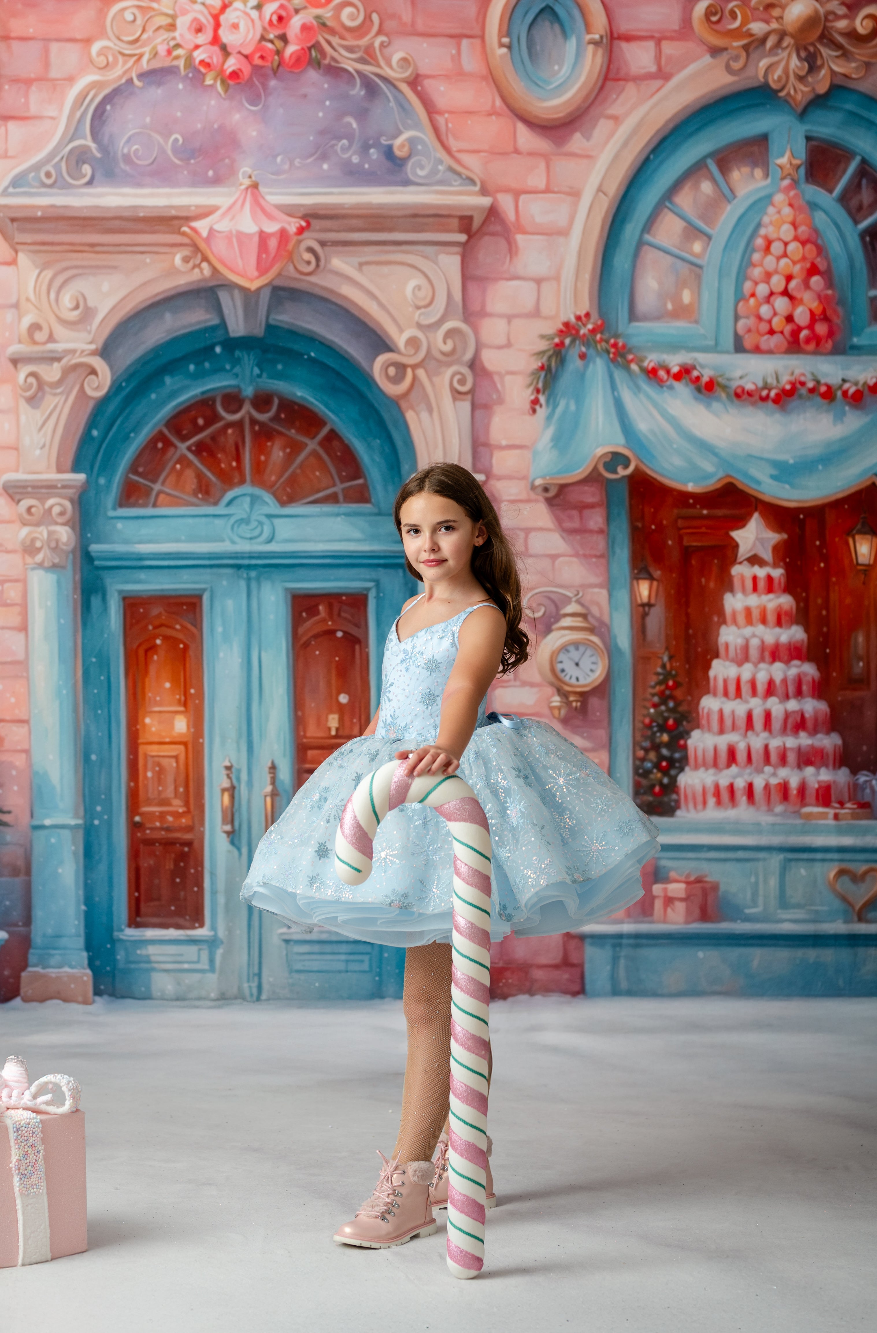 Young girl in a fairy-tale setting with a candy cane, standing in front of a colorful building.