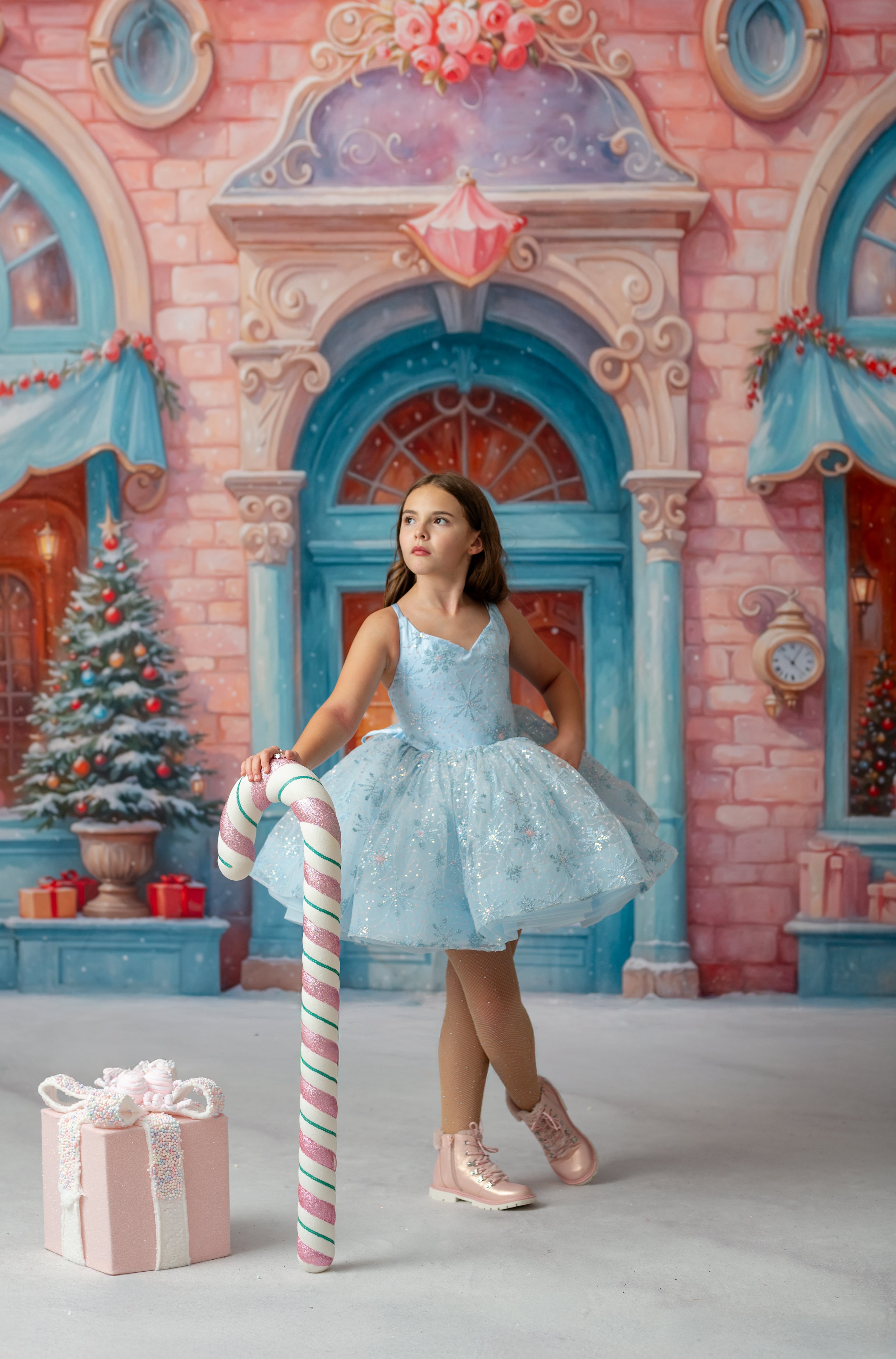 Young girl in a blue dress holding a candy cane in front of a festive castle background