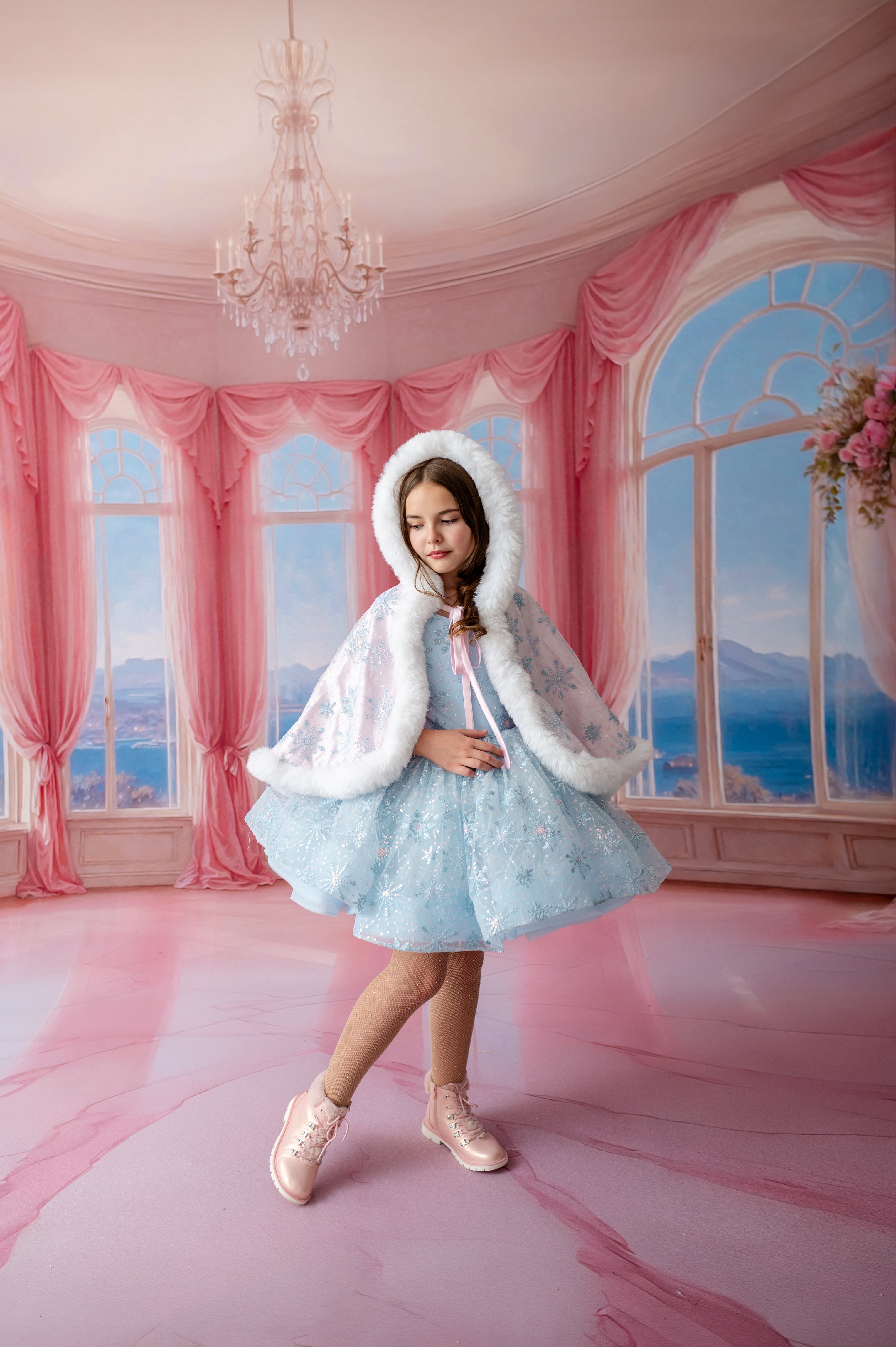 Young girl in a light blue dress with a white fur coat in a pink room with large windows.