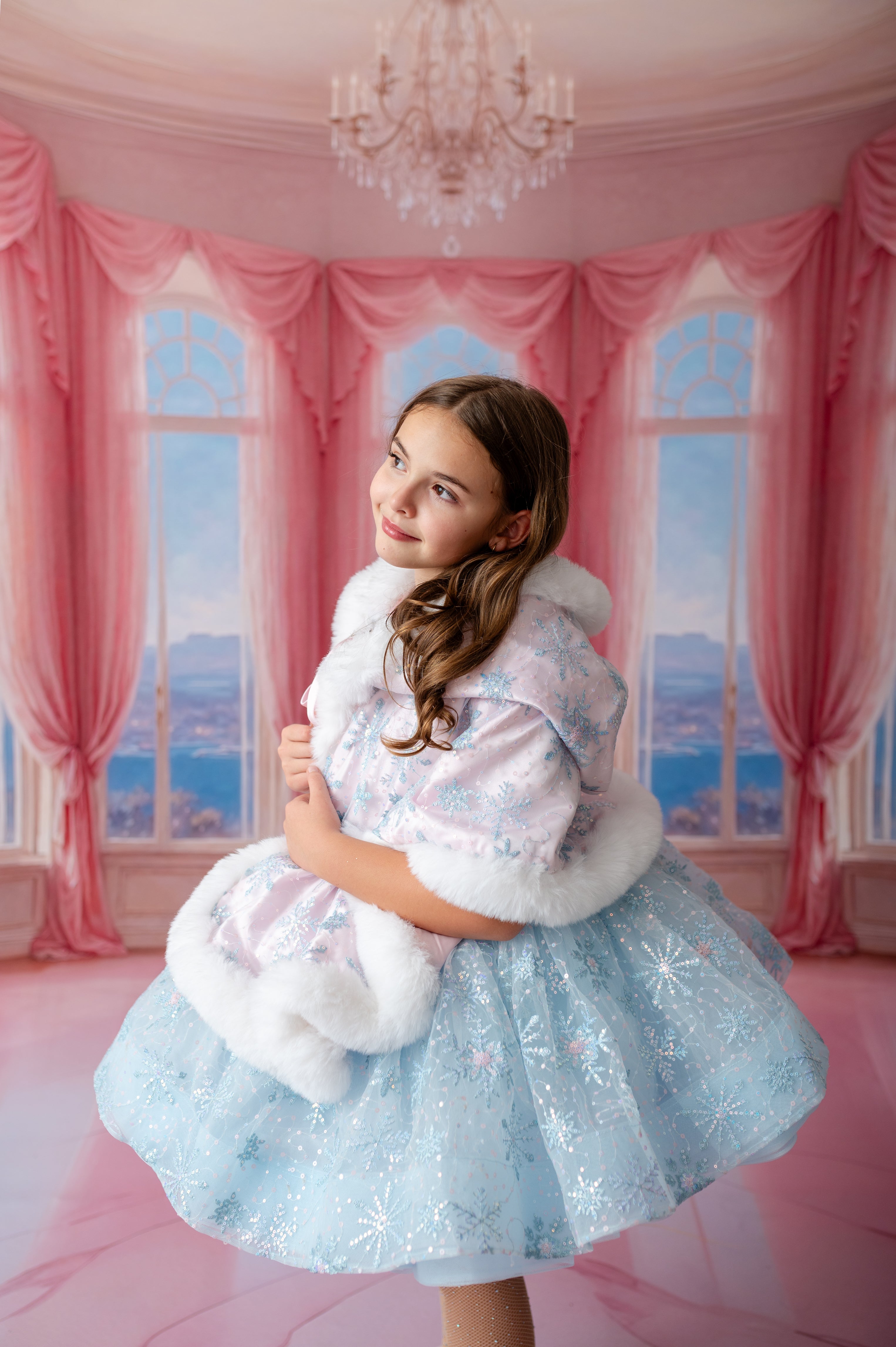 Young girl in a light blue dress with white fur trim in a pink room with chandelier