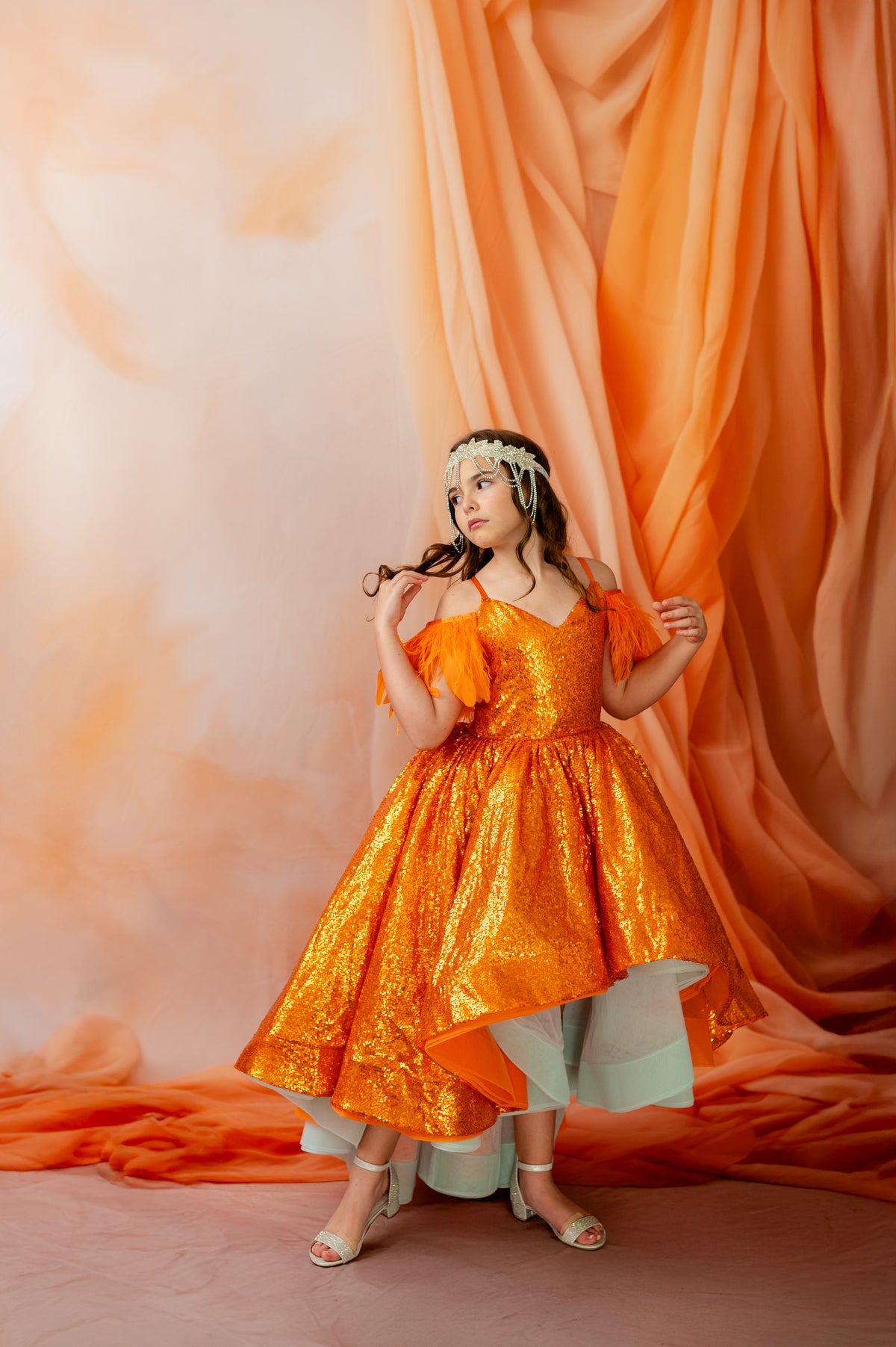 Woman in an orange dress standing against a peach-colored curtain