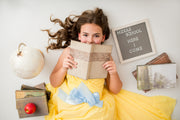 Young girl in a yellow dress holding a book with school-themed decorations around her.