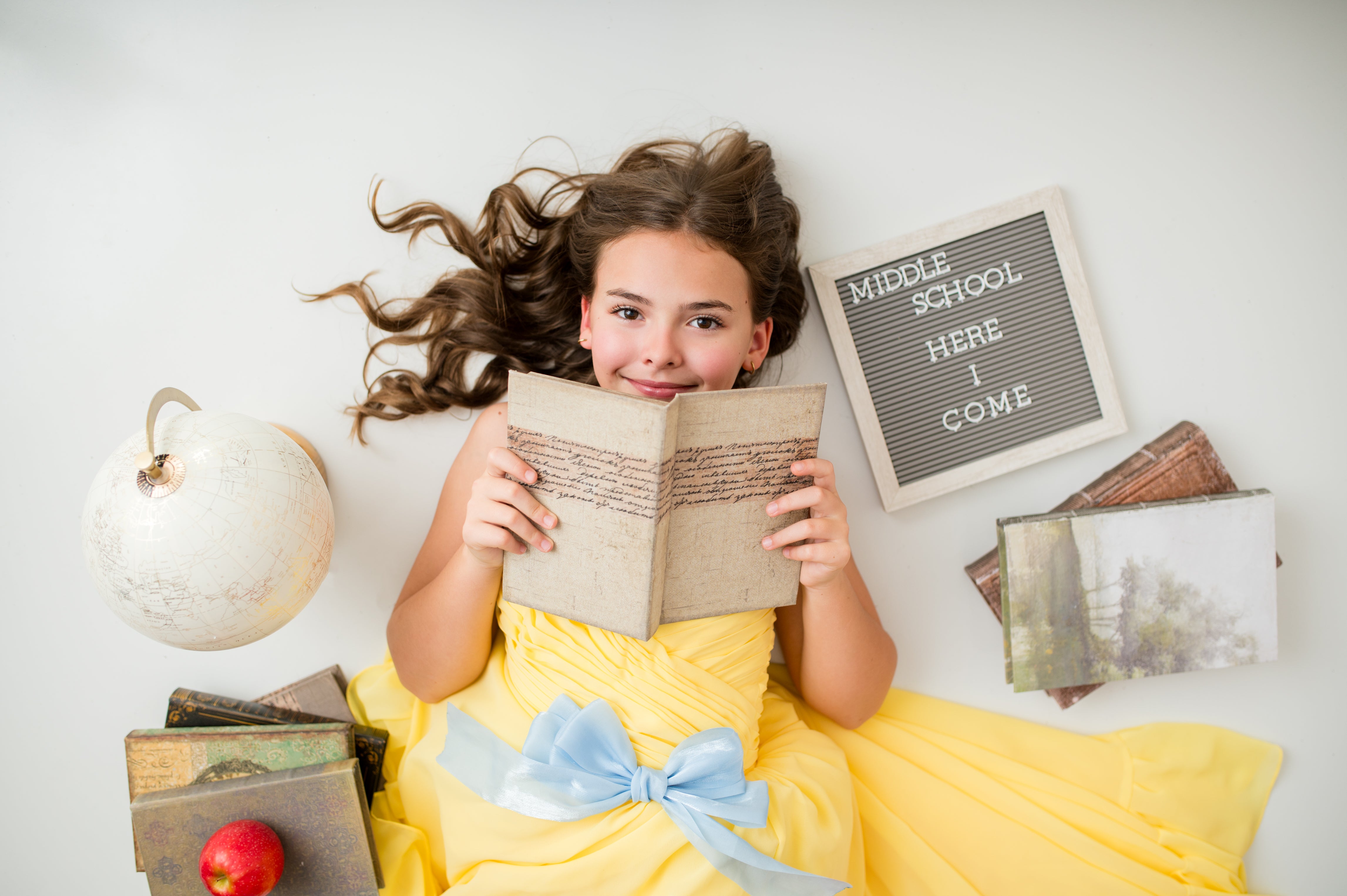 Young girl in a yellow dress holding a book with decorative items around her on a light background