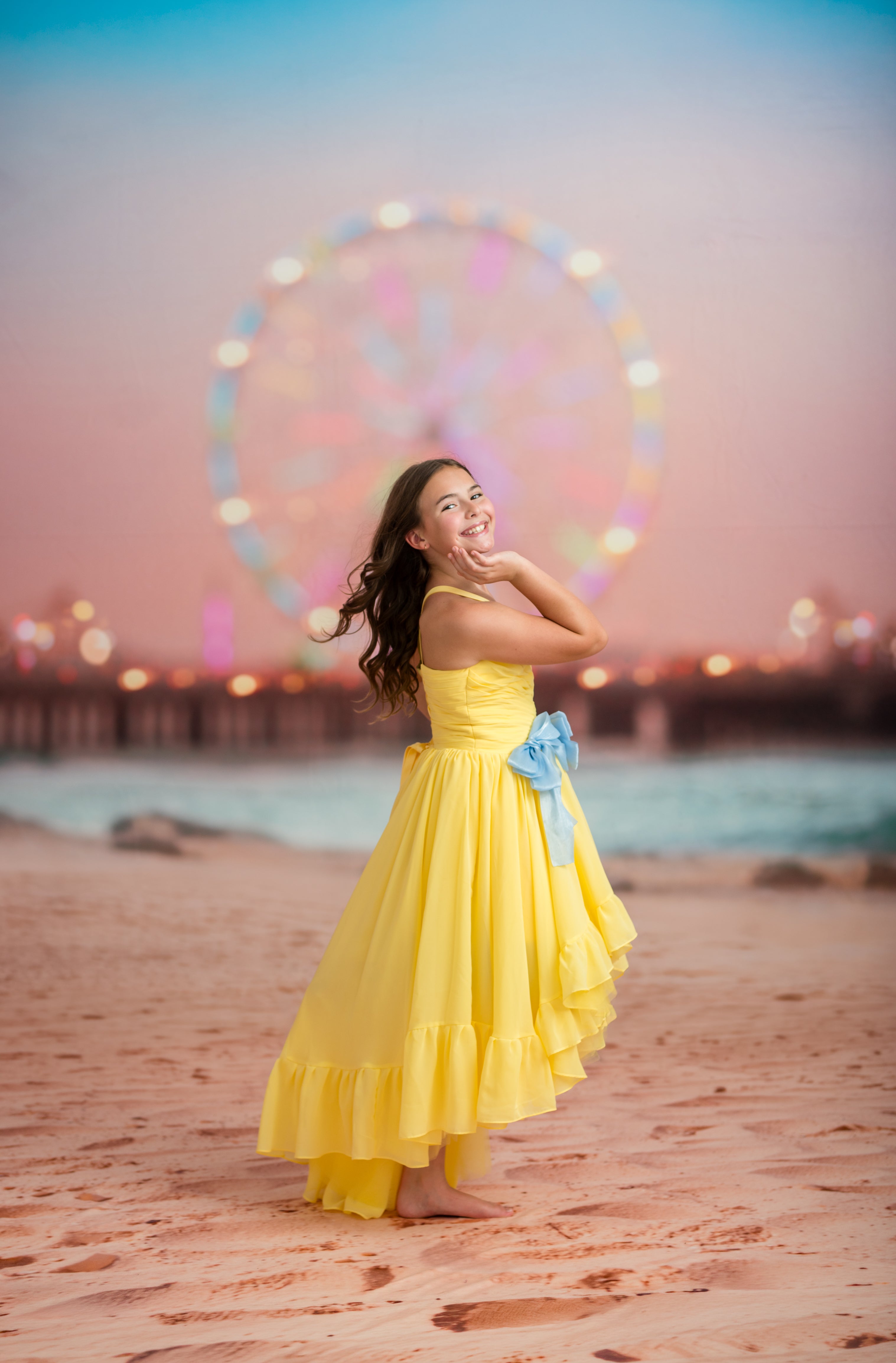 Woman in a yellow dress standing on a beach with a Ferris wheel in the background