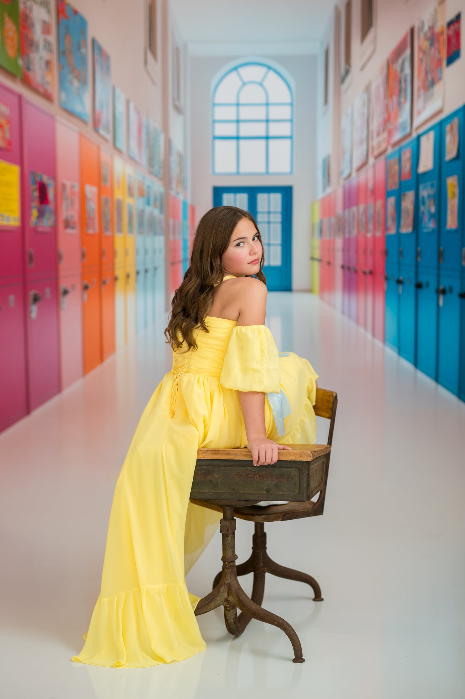 Young woman in a yellow dress sitting on a wooden chair in a colorful hallway.